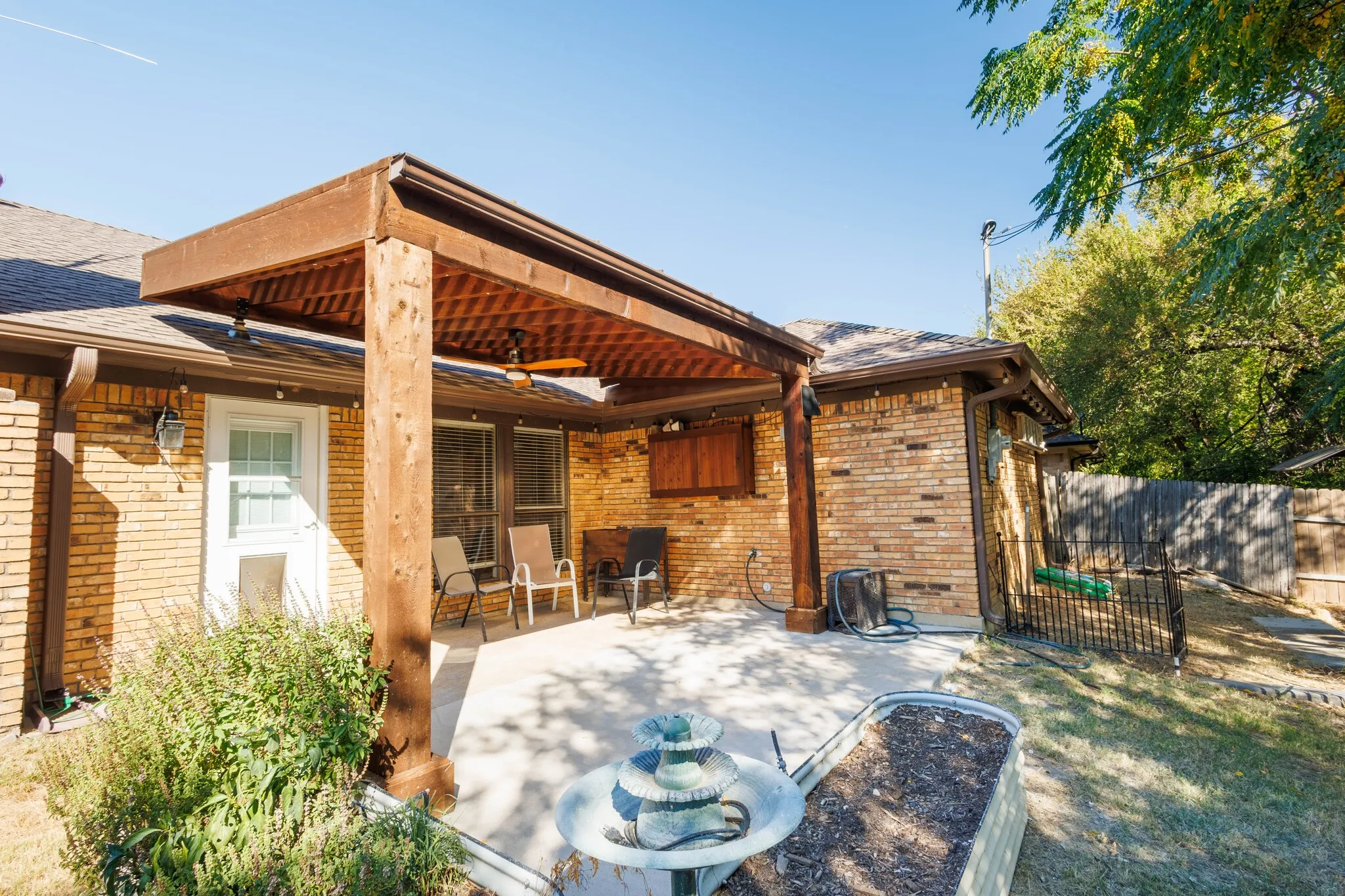 Expansive brick exterior featuring a covered patio with a wood beam ceiling, concrete flooring, and an outdoor ceiling fan