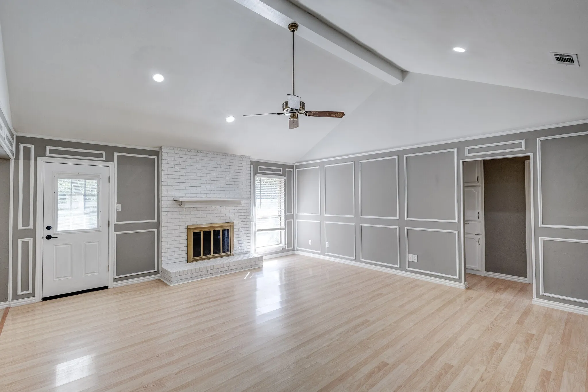 Vaulted ceiling with exposed beam, whitewashed brick fireplace, decorative wall molding, wood-finish flooring, and recessed lighting