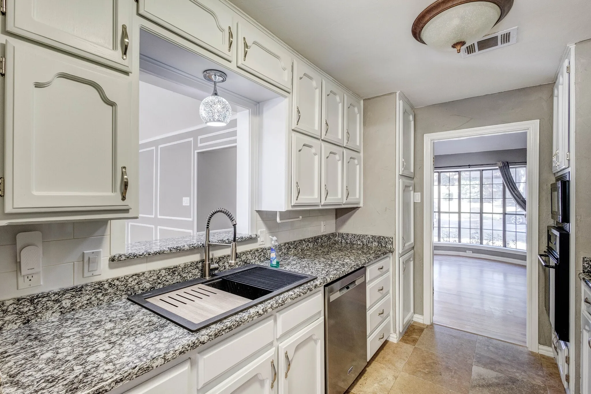 Recessed panel cabinetry, granite-patterned countertops, stainless steel dishwasher, integrated dual wall ovens, and tile flooring