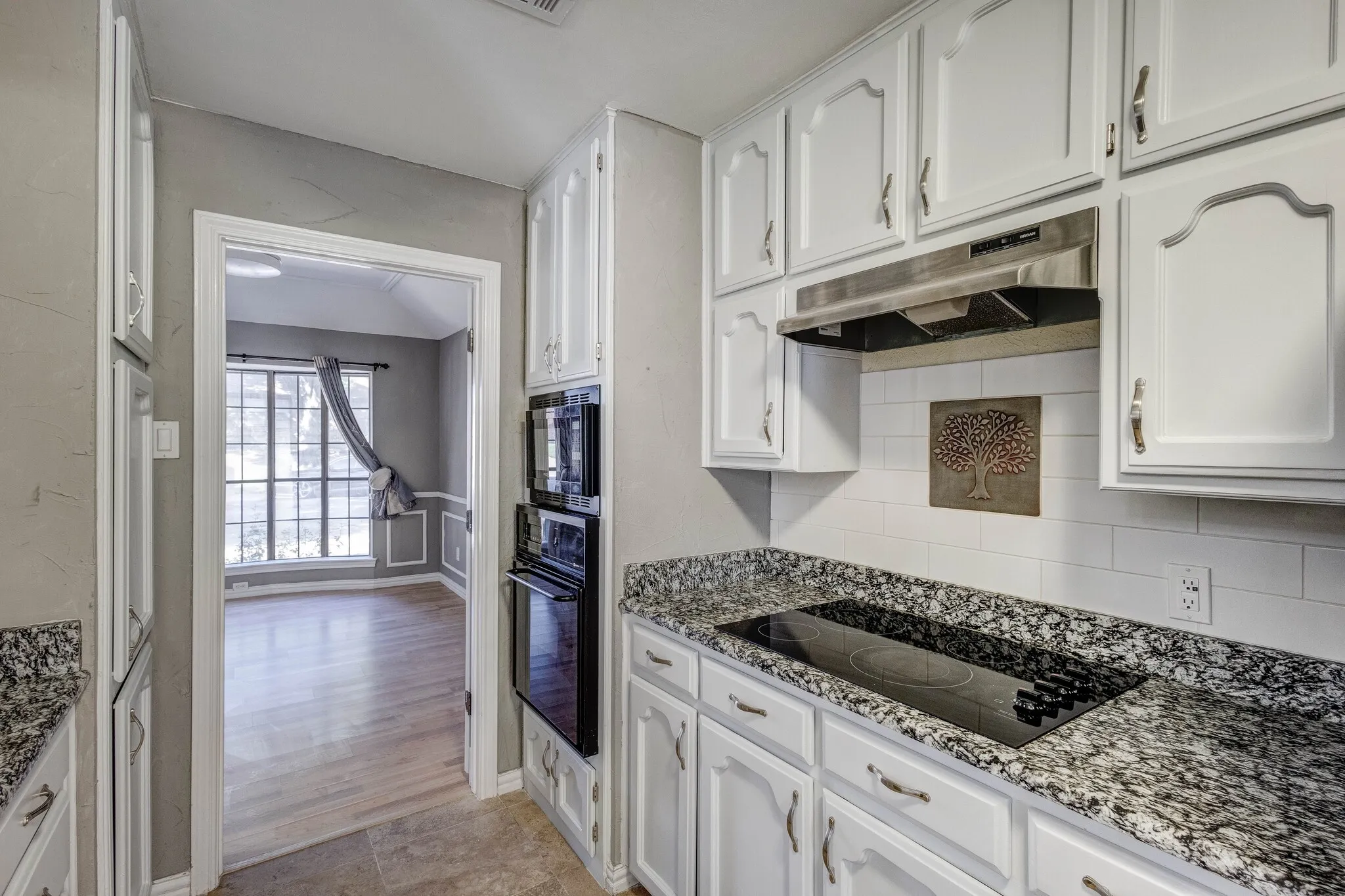White cabinetry with brushed nickel hardware, built-in double ovens, granite-finish countertops, and a subway tile backsplash