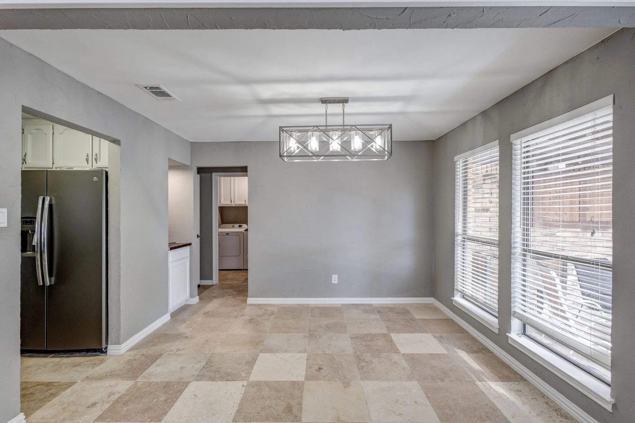 Rectangular tile flooring, two large windows with blinds, and a linear chandelier
