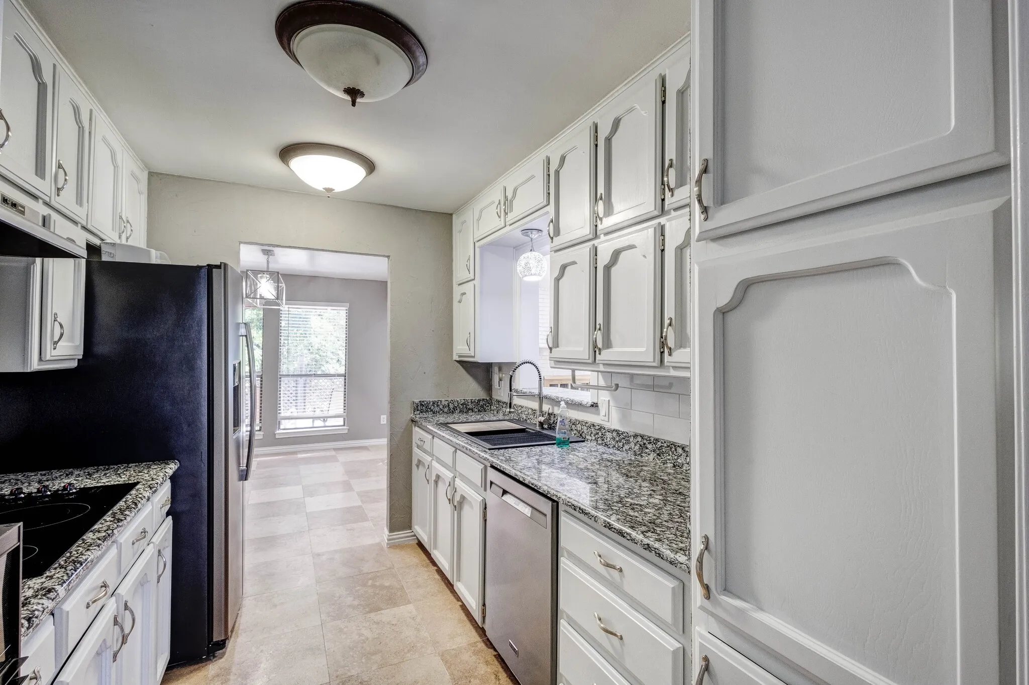 White cabinetry with decorative fronts, speckled countertops, stainless steel dishwasher, tile flooring, and a white subway tile backsplash
