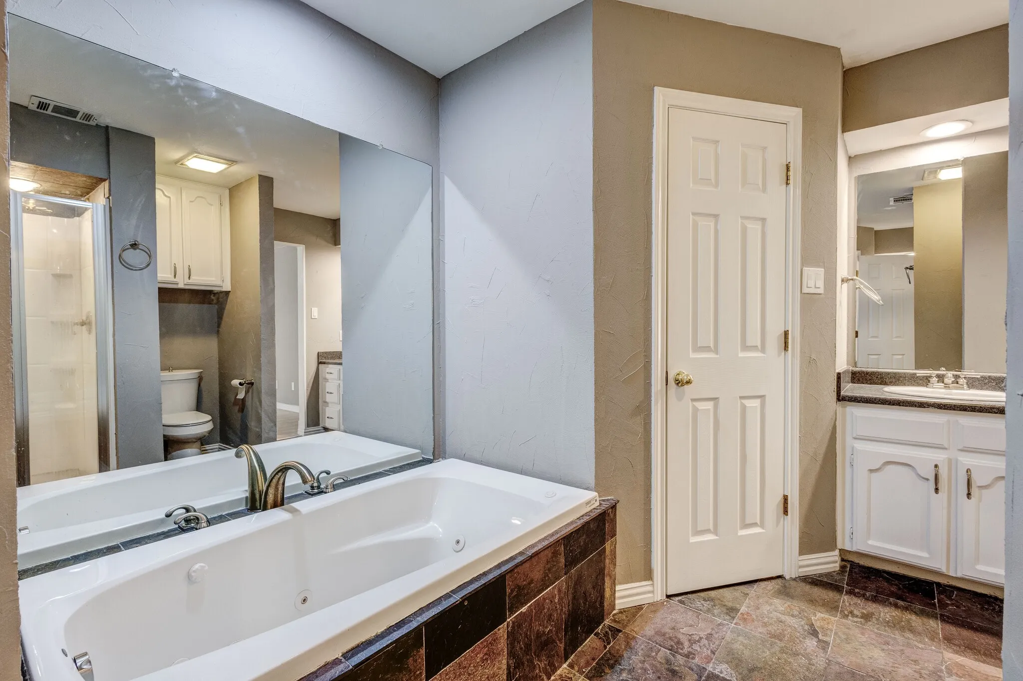 Soaking tub with tile surround, full-width mirror, white vanity with integrated sink, and patterned floor tile