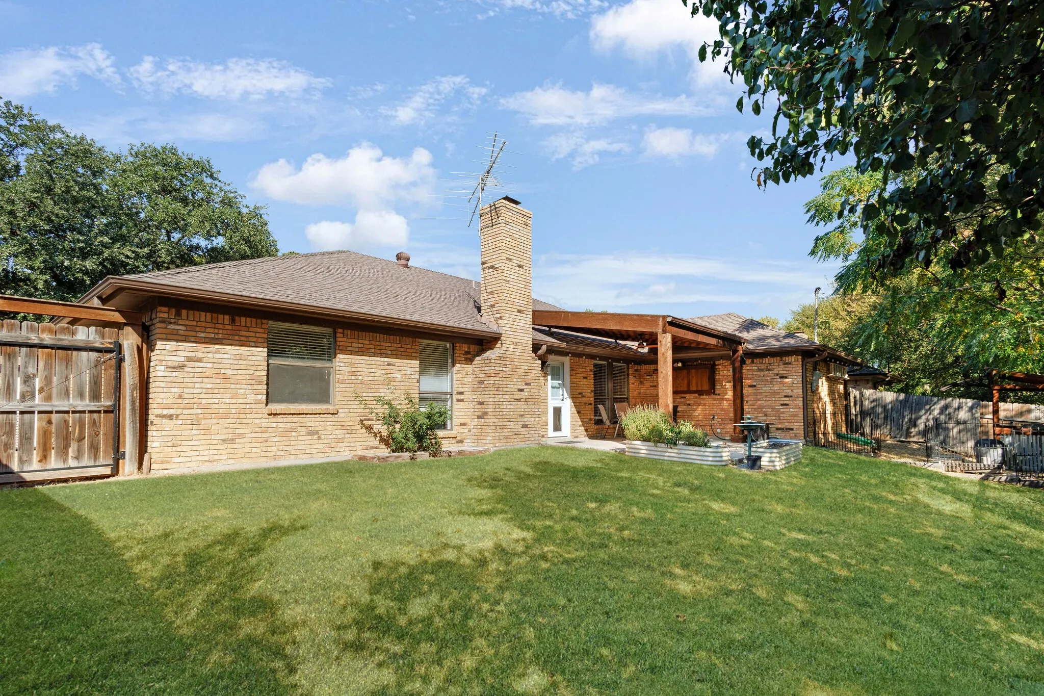 Expansive backyard with a manicured lawn, brick exterior, and a wood pergola