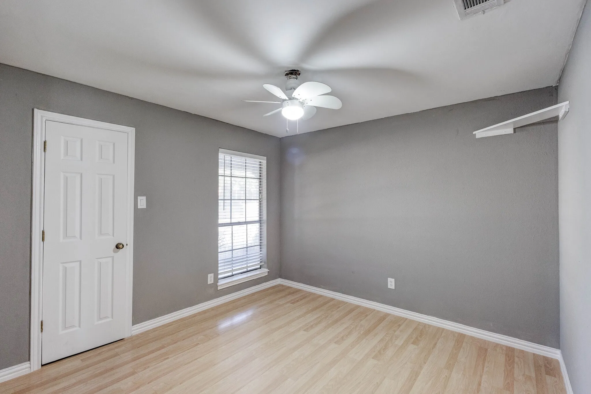 Light wood-finish flooring with white baseboards, a ceiling fan, and a window with blinds