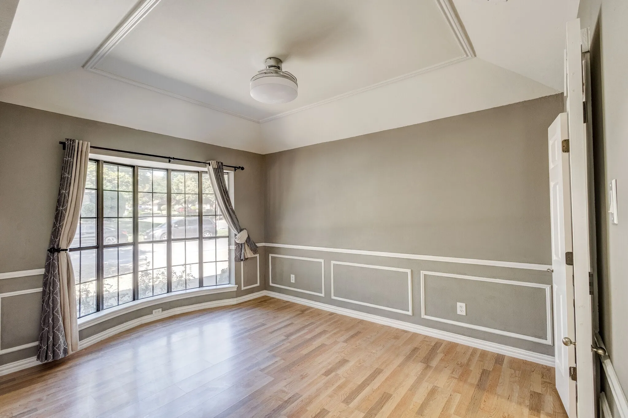 Tray ceiling with recessed lighting, wood-finish flooring, and wainscoting with decorative molding
