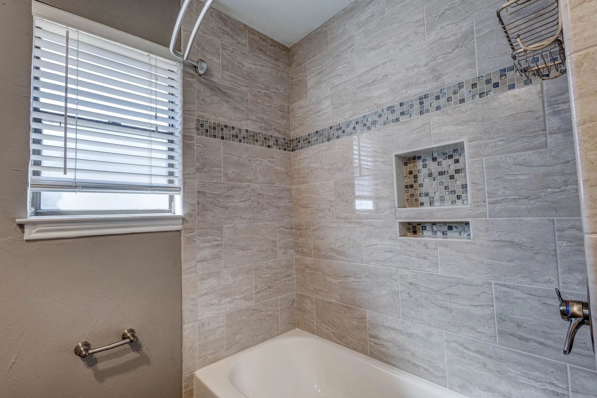 Bathtub with tile surround, mosaic accent band, and integrated tile niches