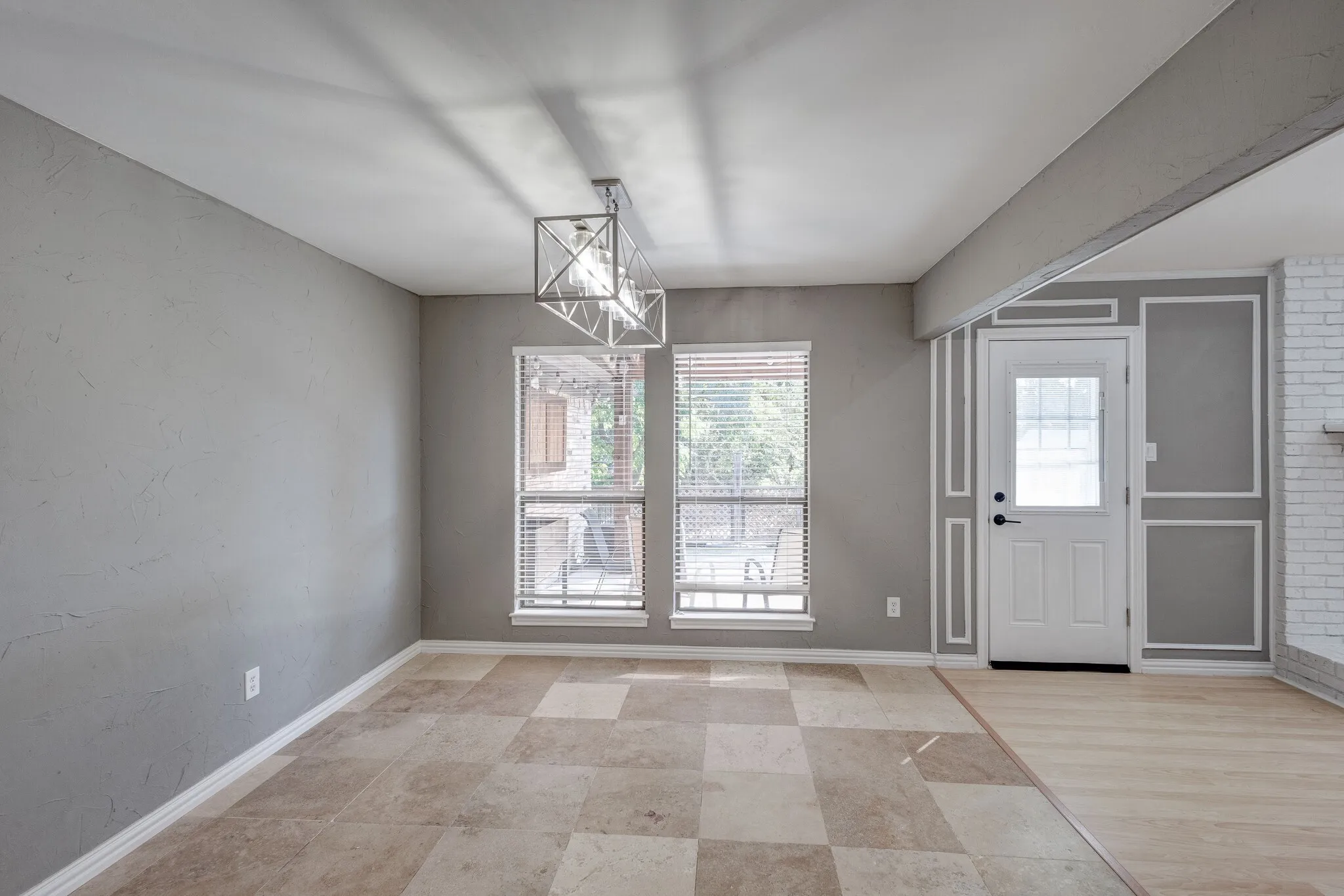 Tiled flooring, dual windows with blinds, modern linear chandelier, decorative wall molding, and a paneled entry door