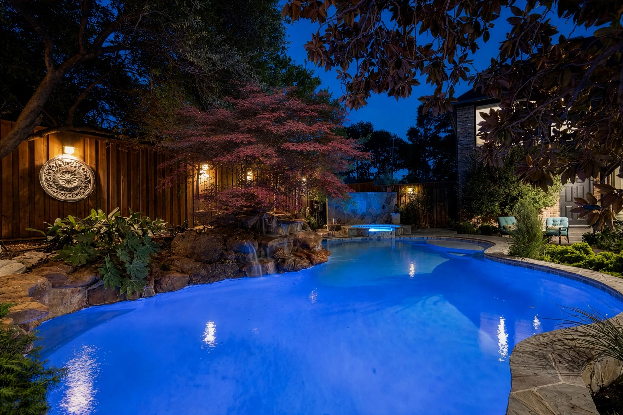 Curved swimming pool with stone coping, rock waterfall feature, and integrated spa
