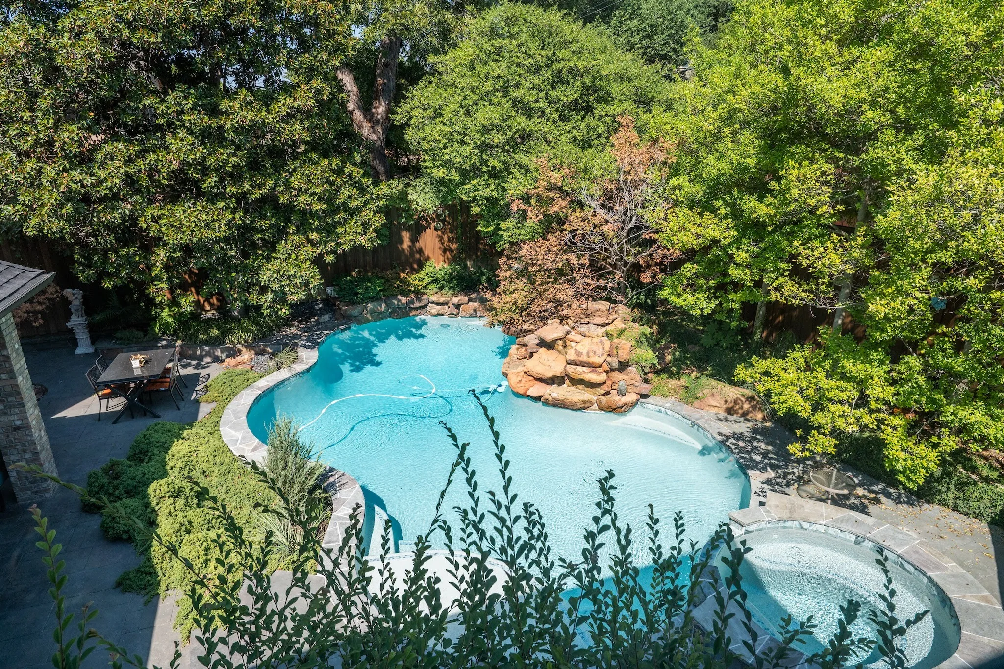 Freeform swimming pool with rock waterfall feature, integrated spa, and surrounding stone decking