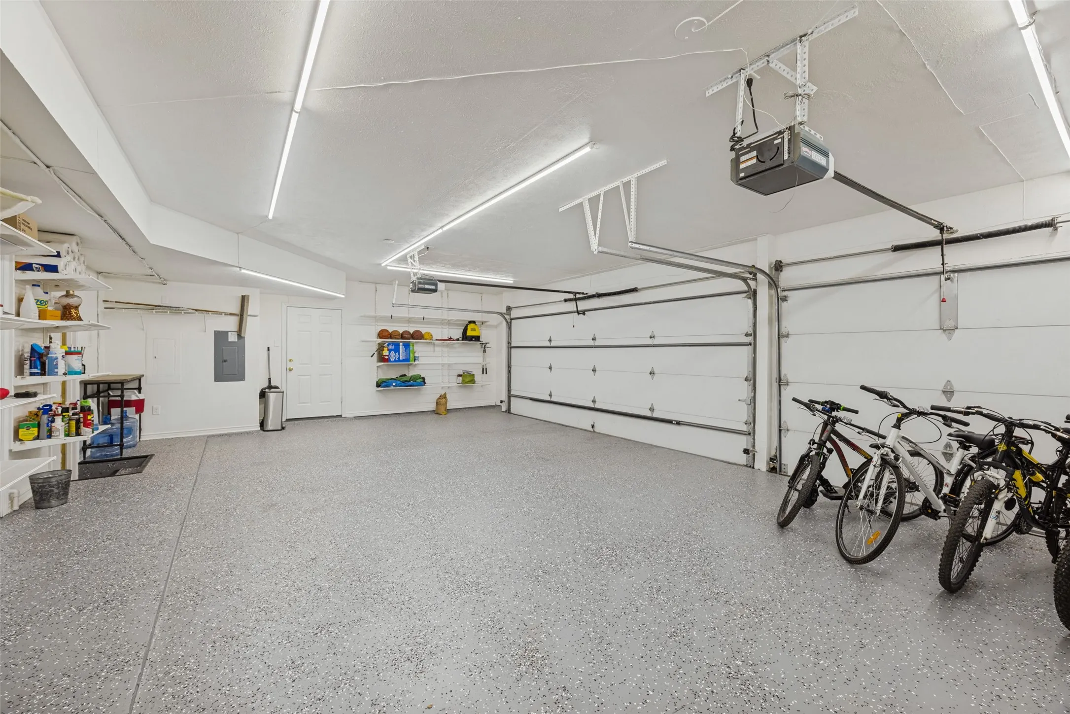 3 car garage featuring a new epoxy floor coating, two overhead garage doors, overhead garage door opener, and built-in elfa shelving, fresh paint, new track lightings