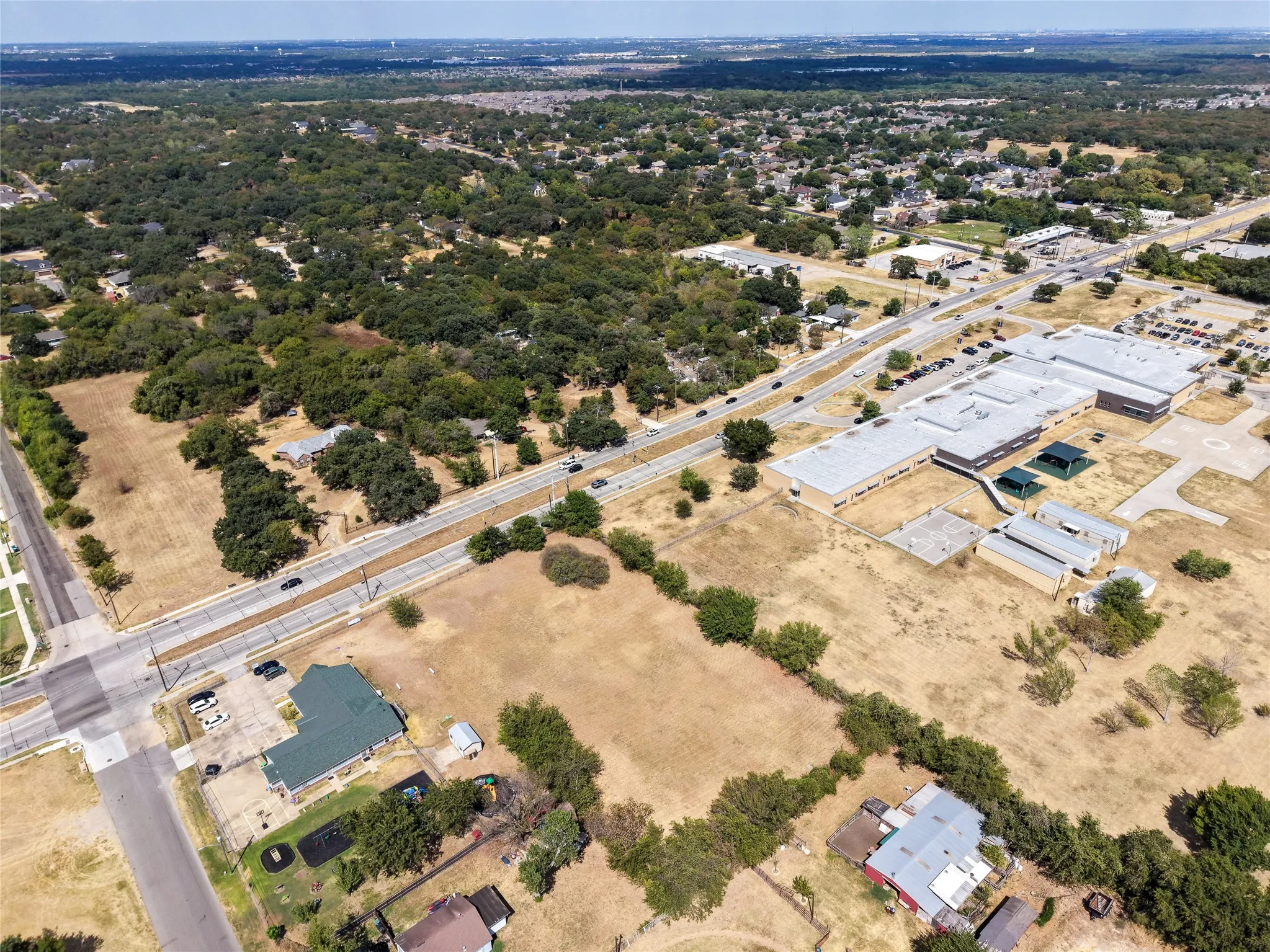 Aerial perspective showcasing a developed area with extensive tree coverage, roadways, and multiple buildings