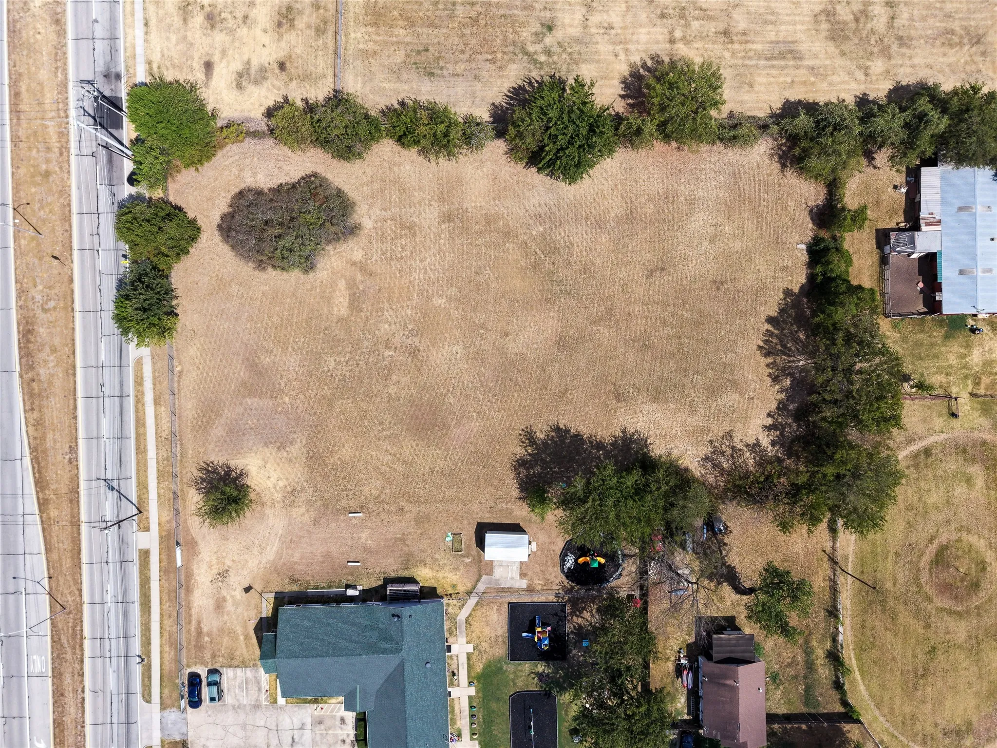 Expansive land parcel with surrounding mature trees and direct street access