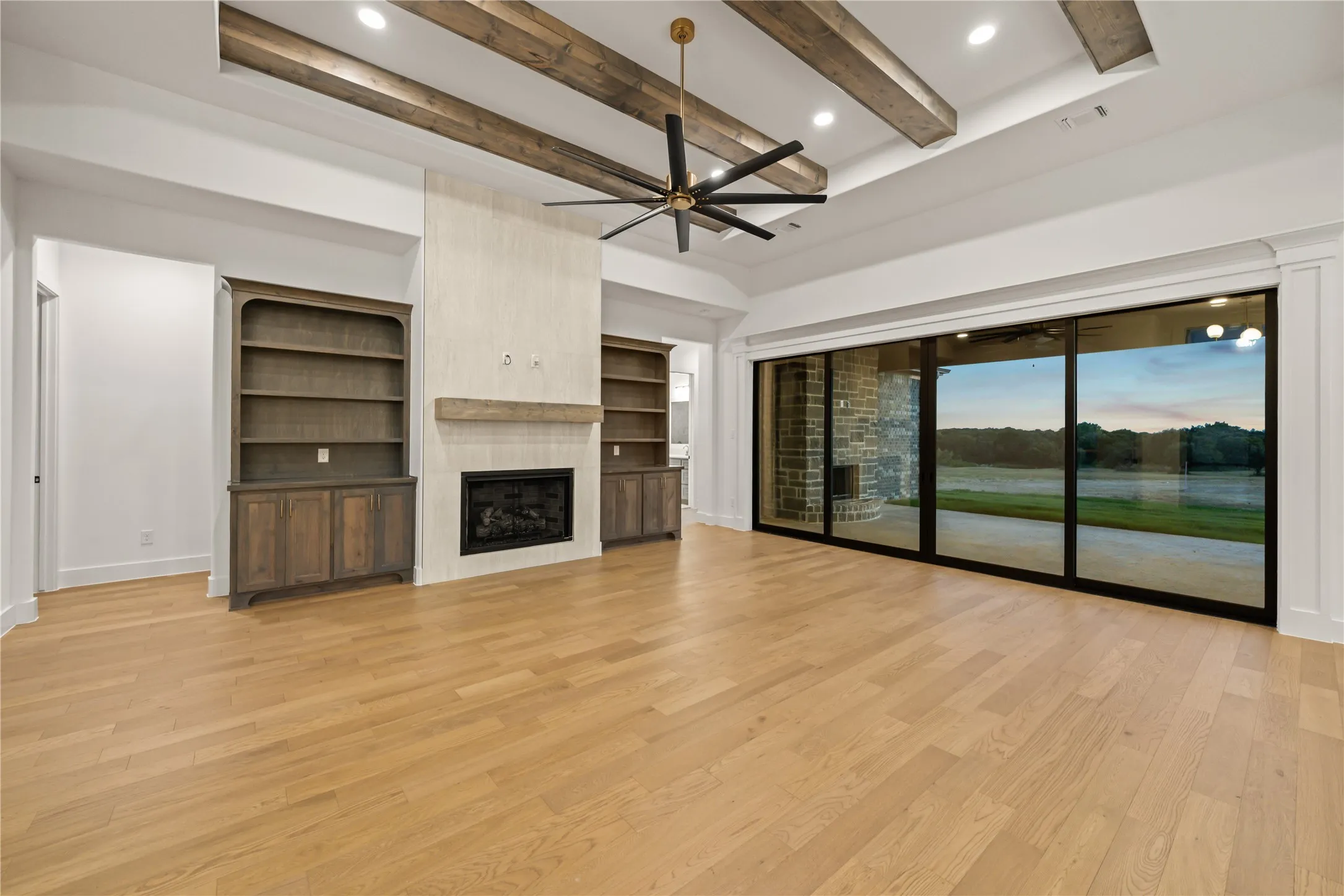 Hardwood flooring, fireplace with a wood mantle, built-in shelving, exposed beam ceiling, and a multi-panel sliding glass door