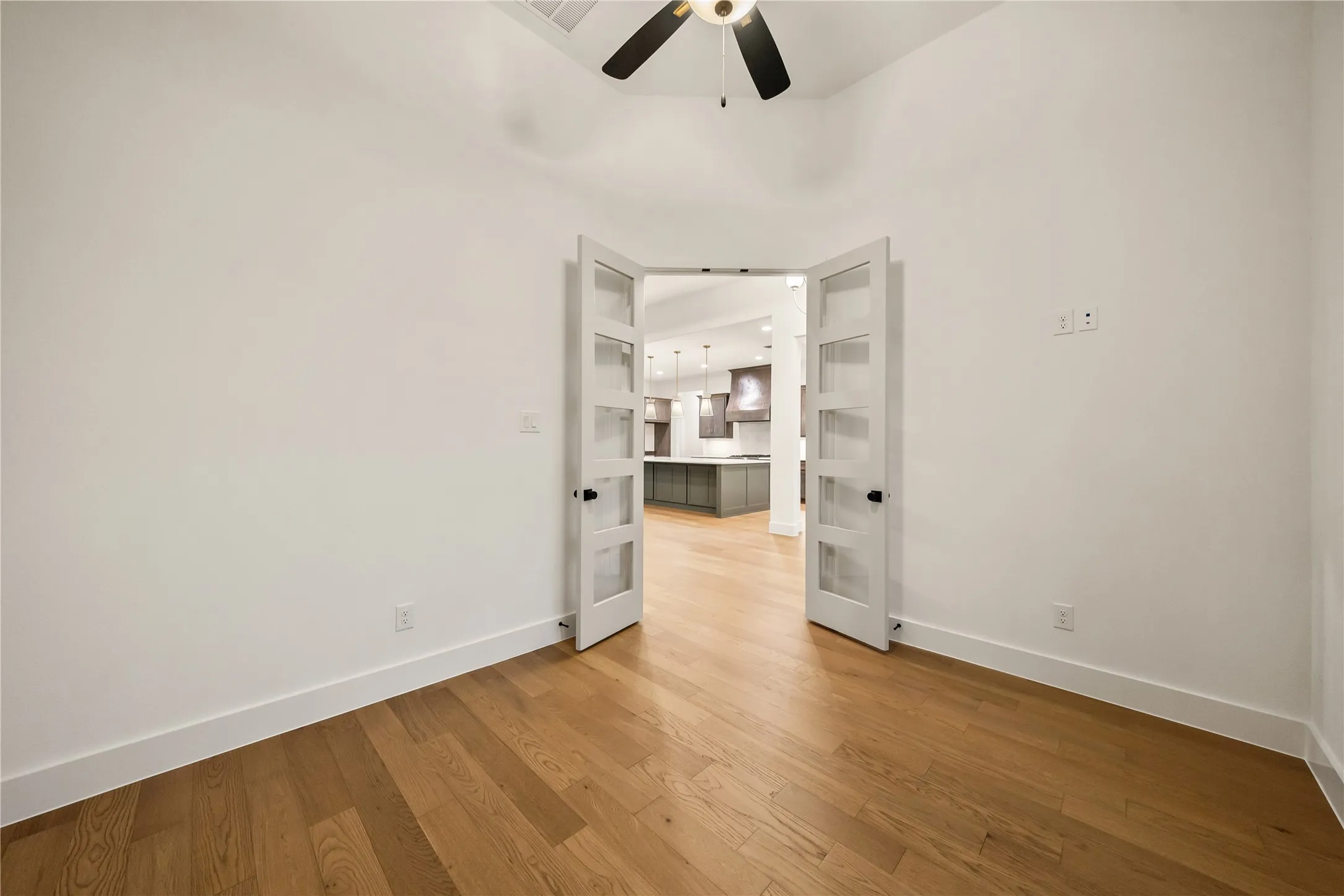 Wood-finish flooring, white walls, and French doors with clear glass panels