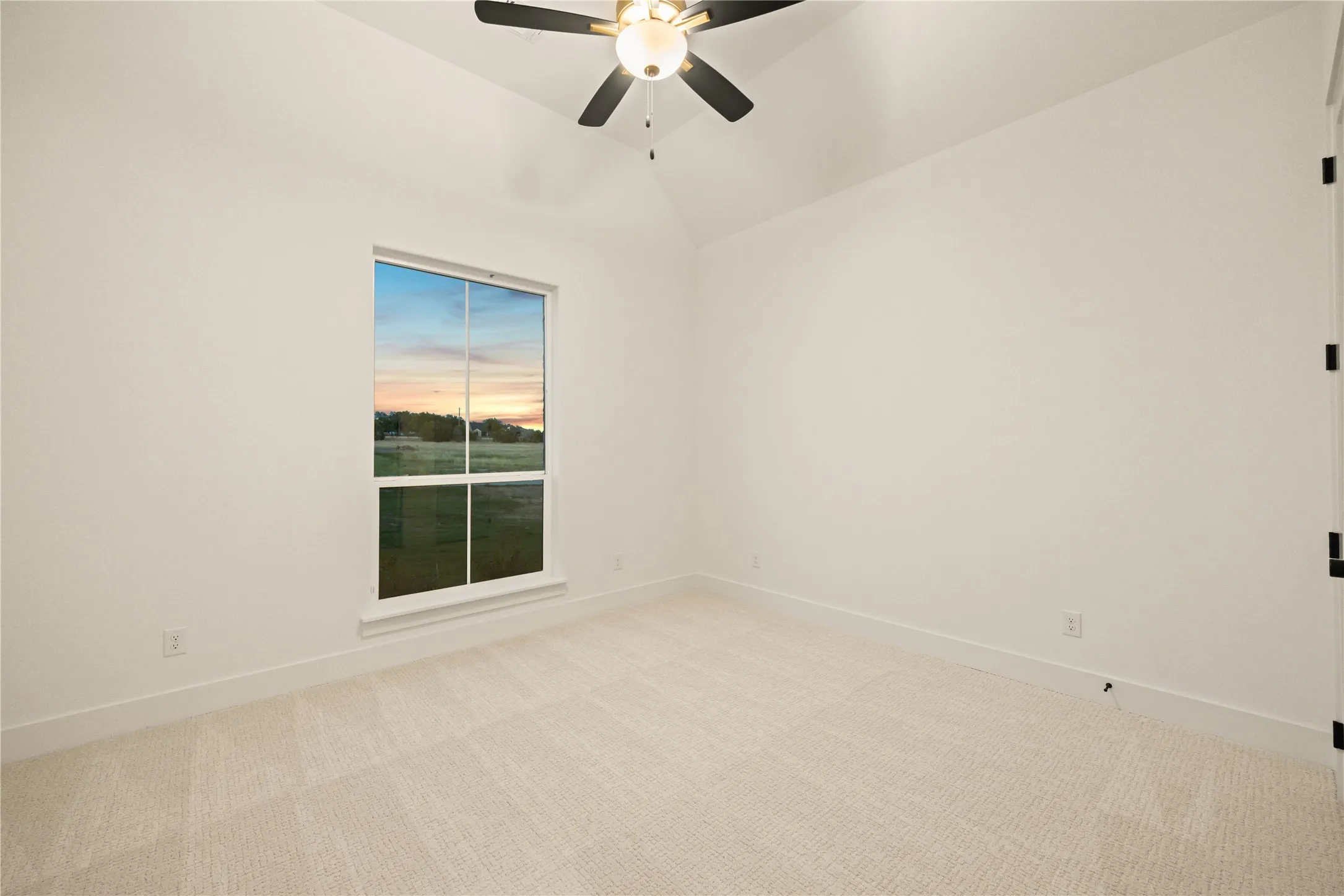 Vaulted ceiling with a ceiling fan, neutral wall paint, light-colored carpet flooring, and a large window
