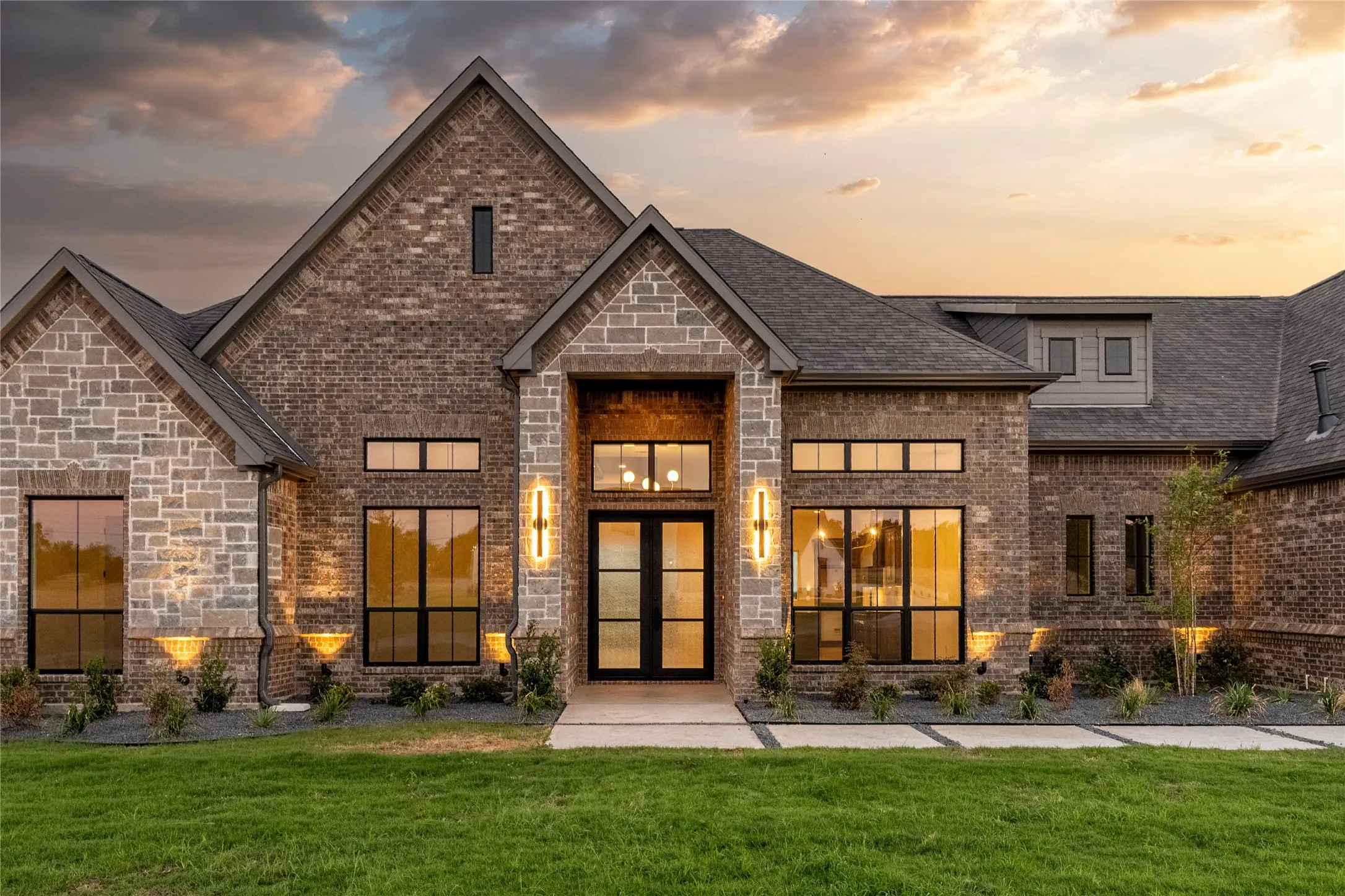 Exterior featuring a combination of brick and stone masonry, multiple gables, a double-door entry, and black-framed windows