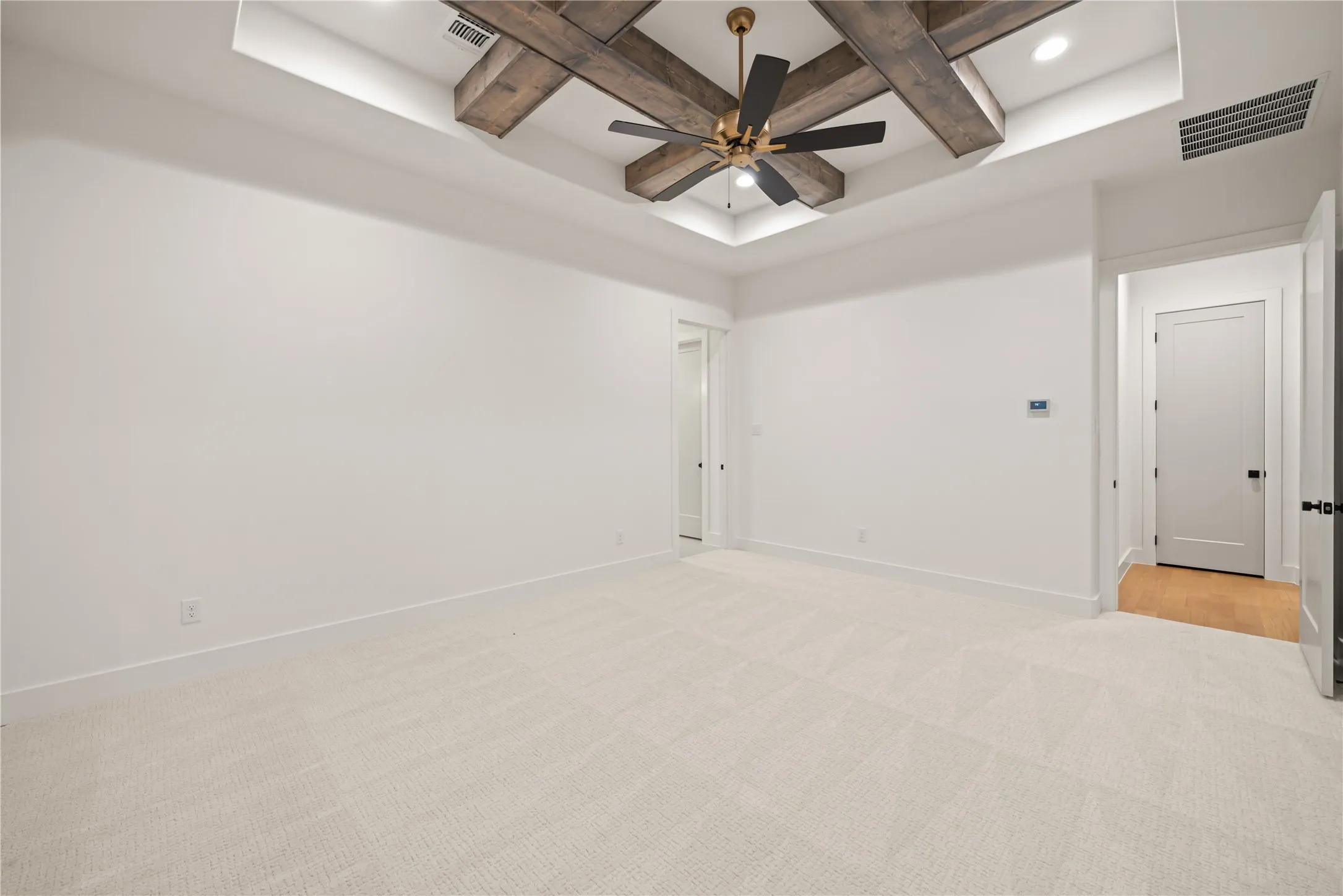 Recessed lighting, a tray ceiling with wood-finish beams, and a ceiling fan with gold-tone accents