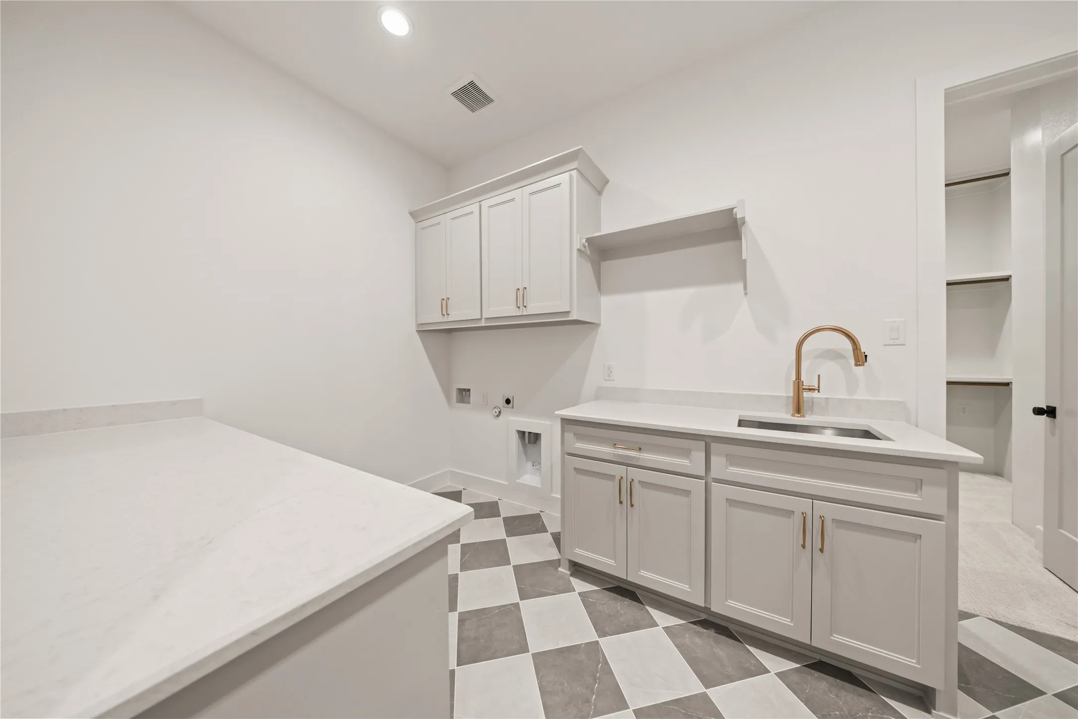 Laundry room featuring checkerboard flooring, light-toned cabinetry, a built-in sink with a gooseneck faucet, and extensive countertop space