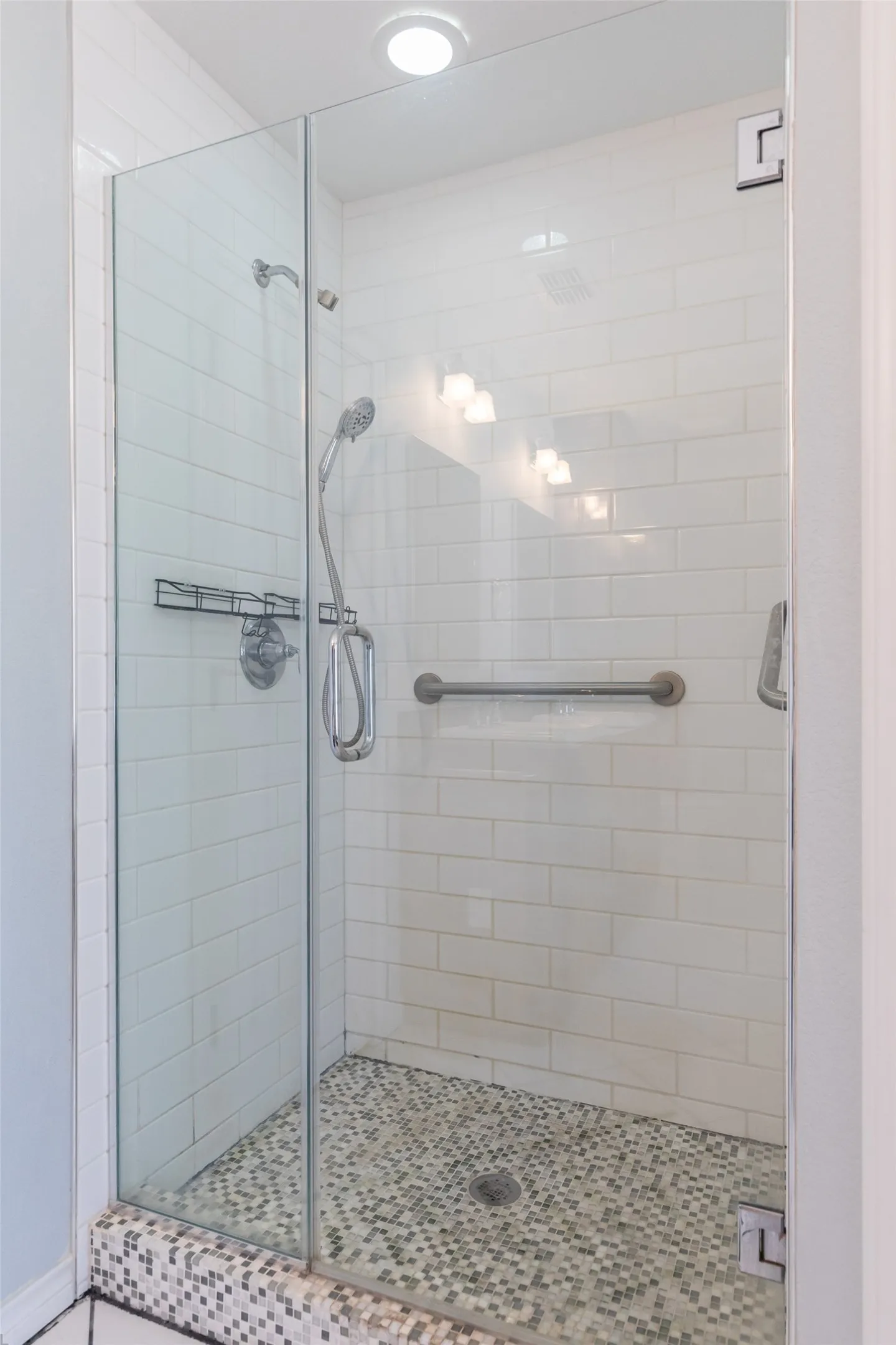 Glass-enclosed shower featuring subway tile walls, pebble-finish flooring, and a chrome grab bar