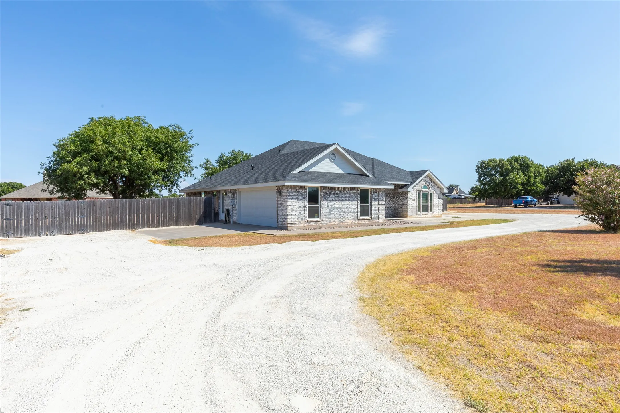 Exterior featuring a brick facade, attached garage, dark shingle roof, and a gravel driveway