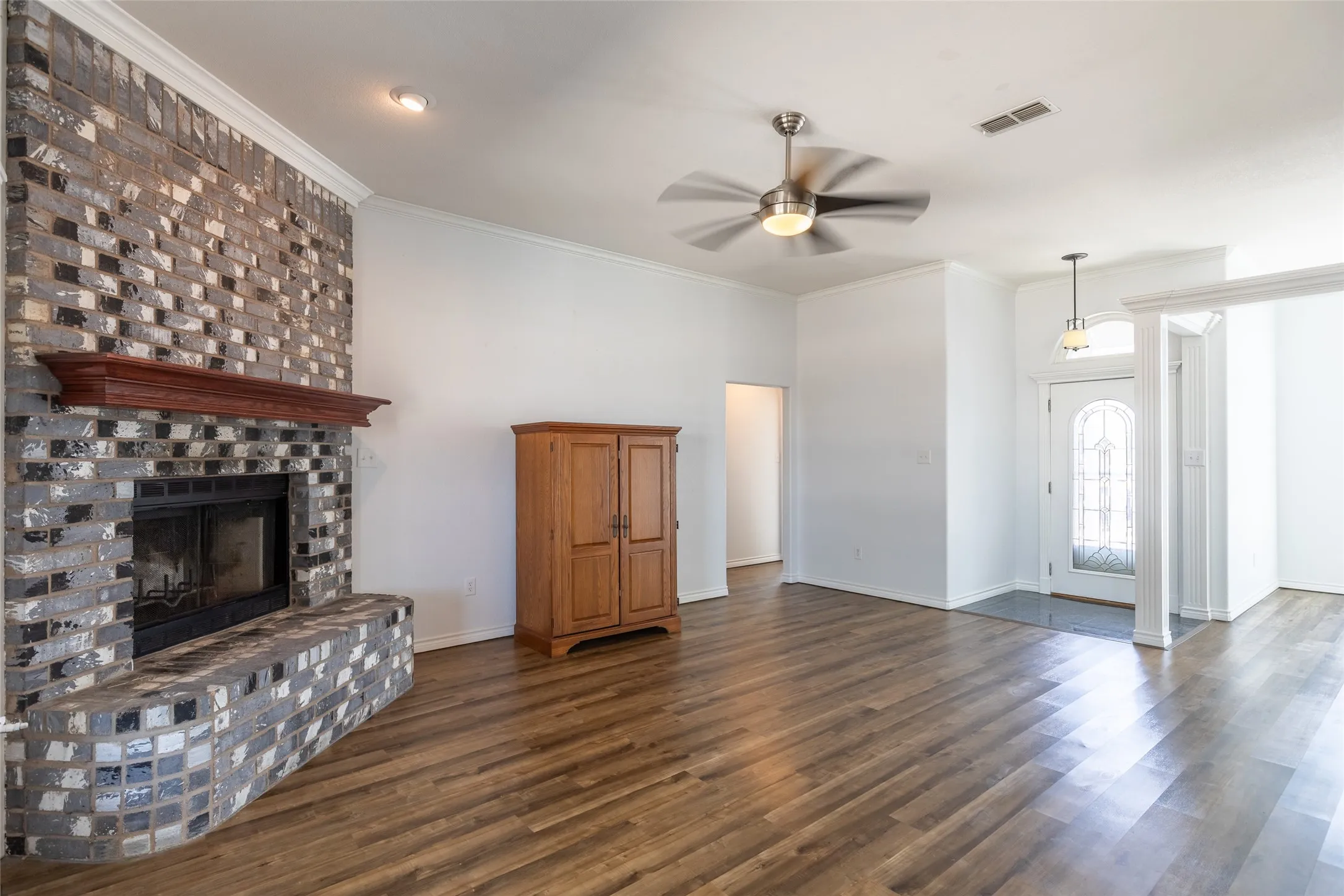 Wood-finish flooring throughout, brick fireplace with a wood mantle, ceiling fan with integrated lighting, recessed lighting, and a front entry door with decorative glass