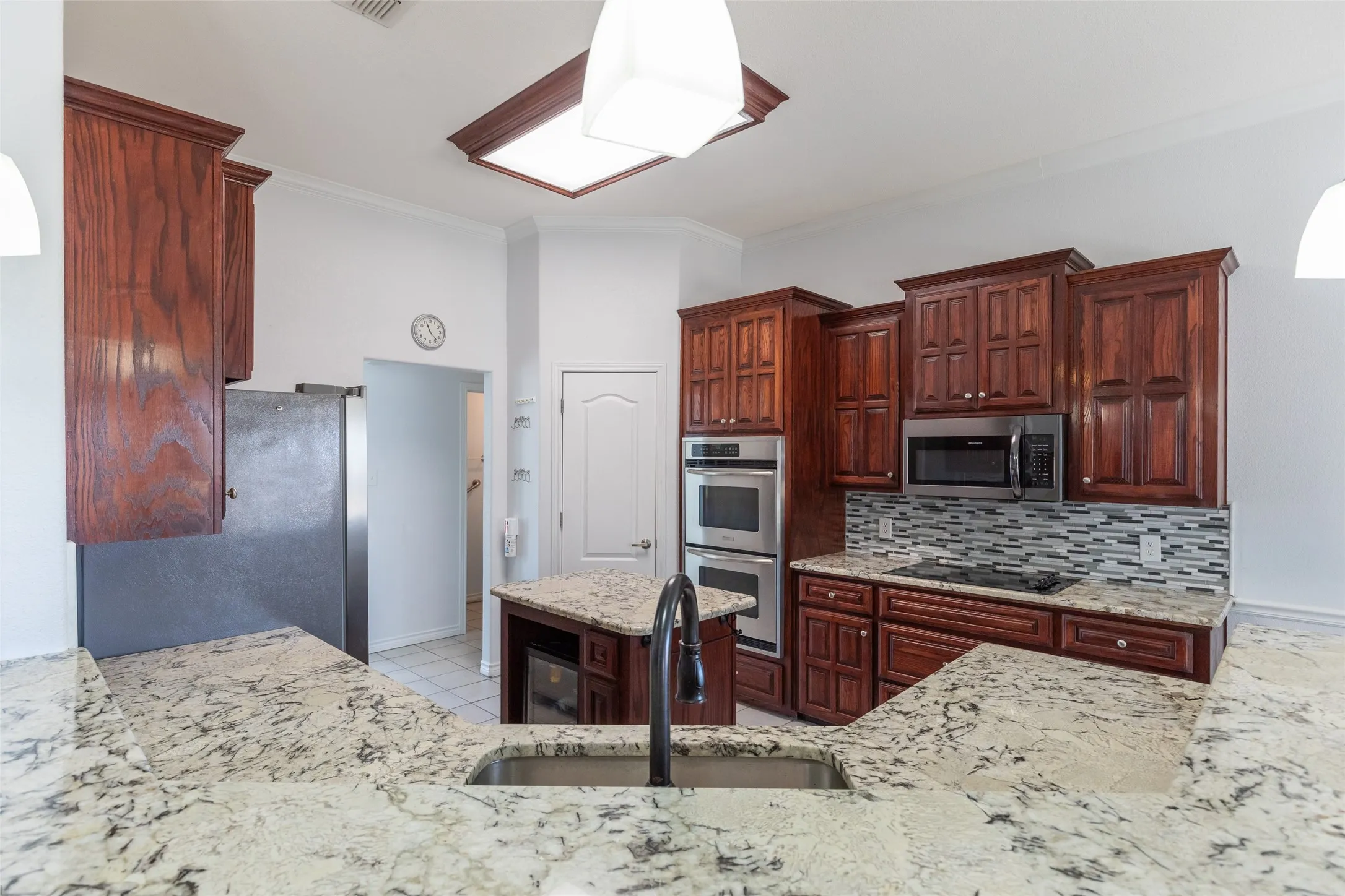 Kitchen featuring expansive countertop space, rich wood-finish cabinetry, stainless steel appliances, a center island, and a decorative tile backsplash