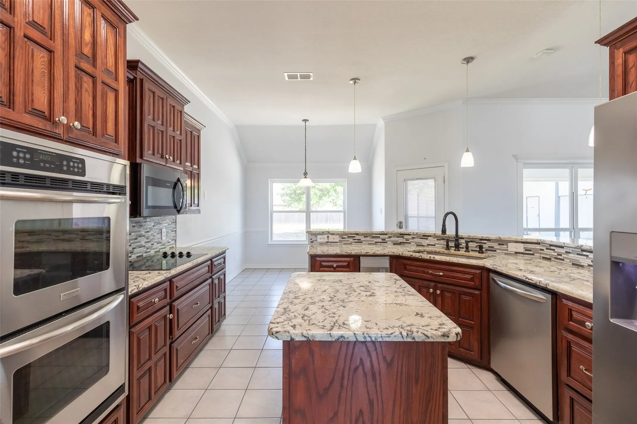 Kitchen featuring wood cabinetry, light-toned stone countertops, stainless steel appliances, and a tile backsplash