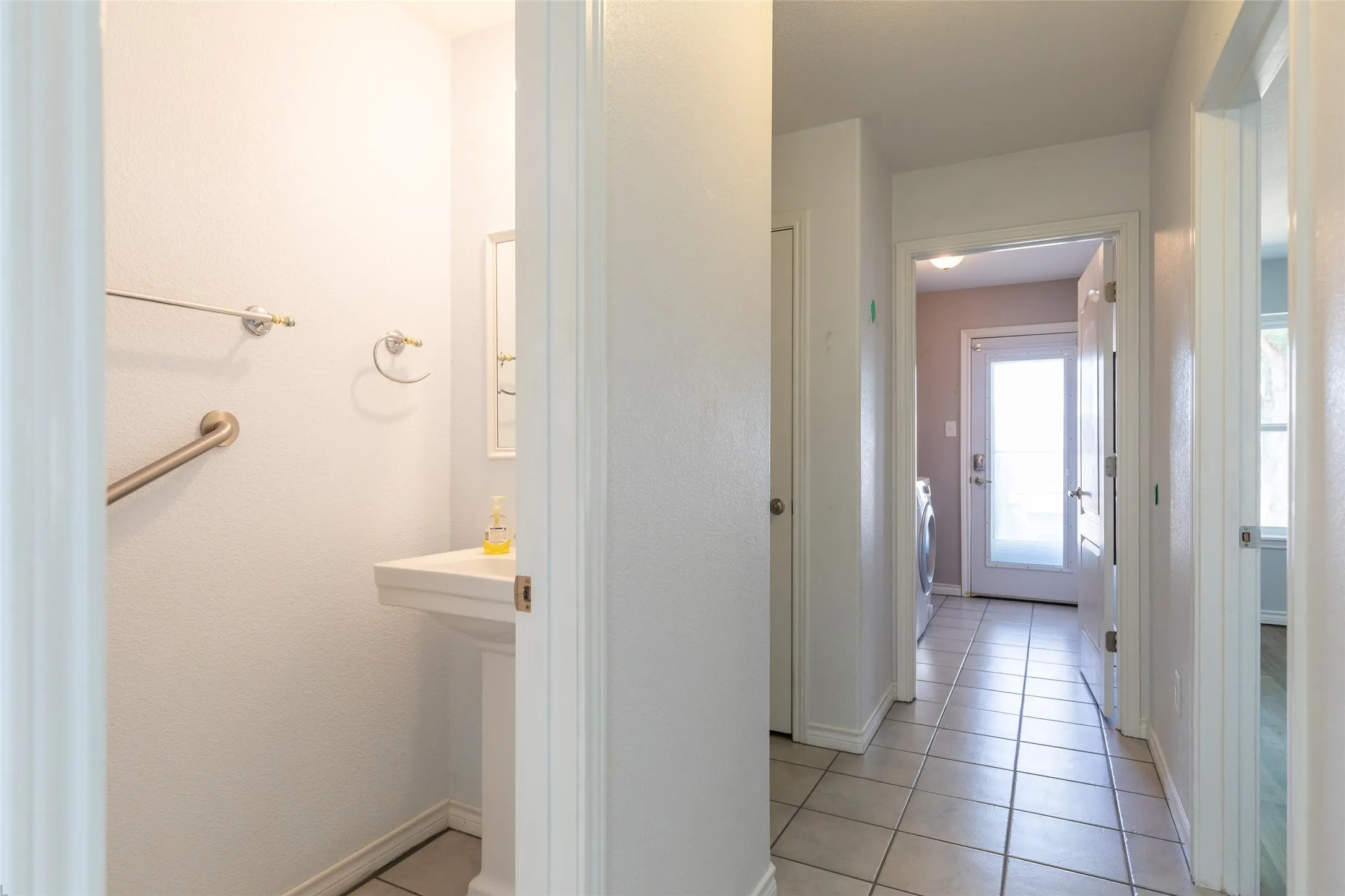 Pedestal sink, wall-mounted mirror, ceramic tile flooring, interior doors, and a frosted glass exterior door