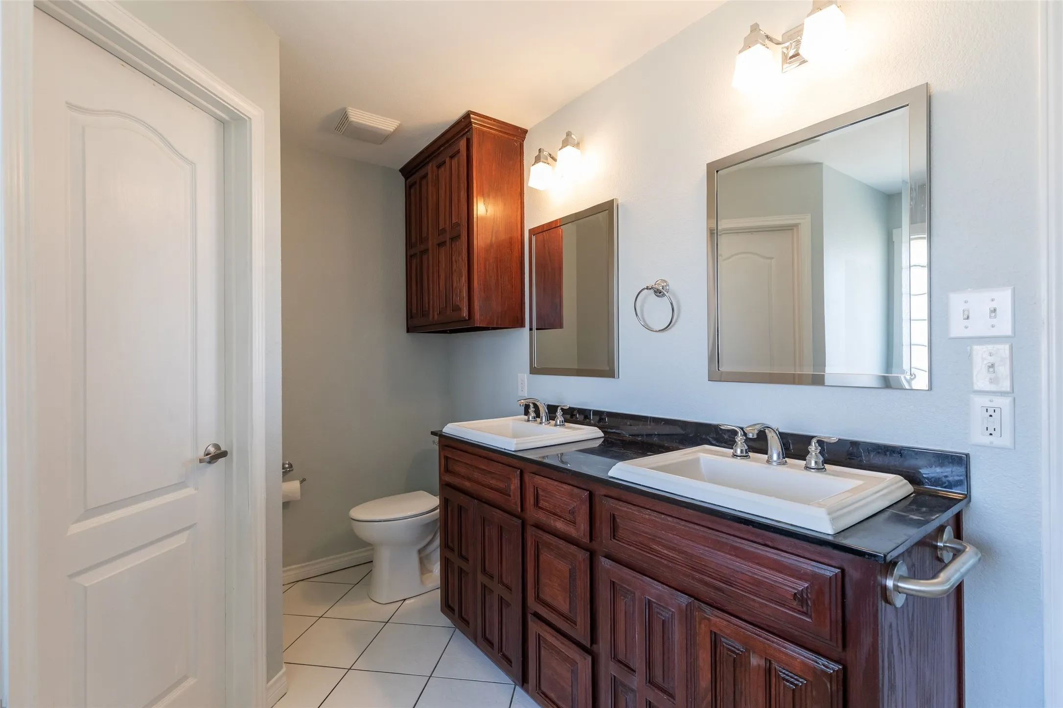 Dual vanity with dark wood cabinetry, integrated sinks, dark countertop, and two framed mirrors
