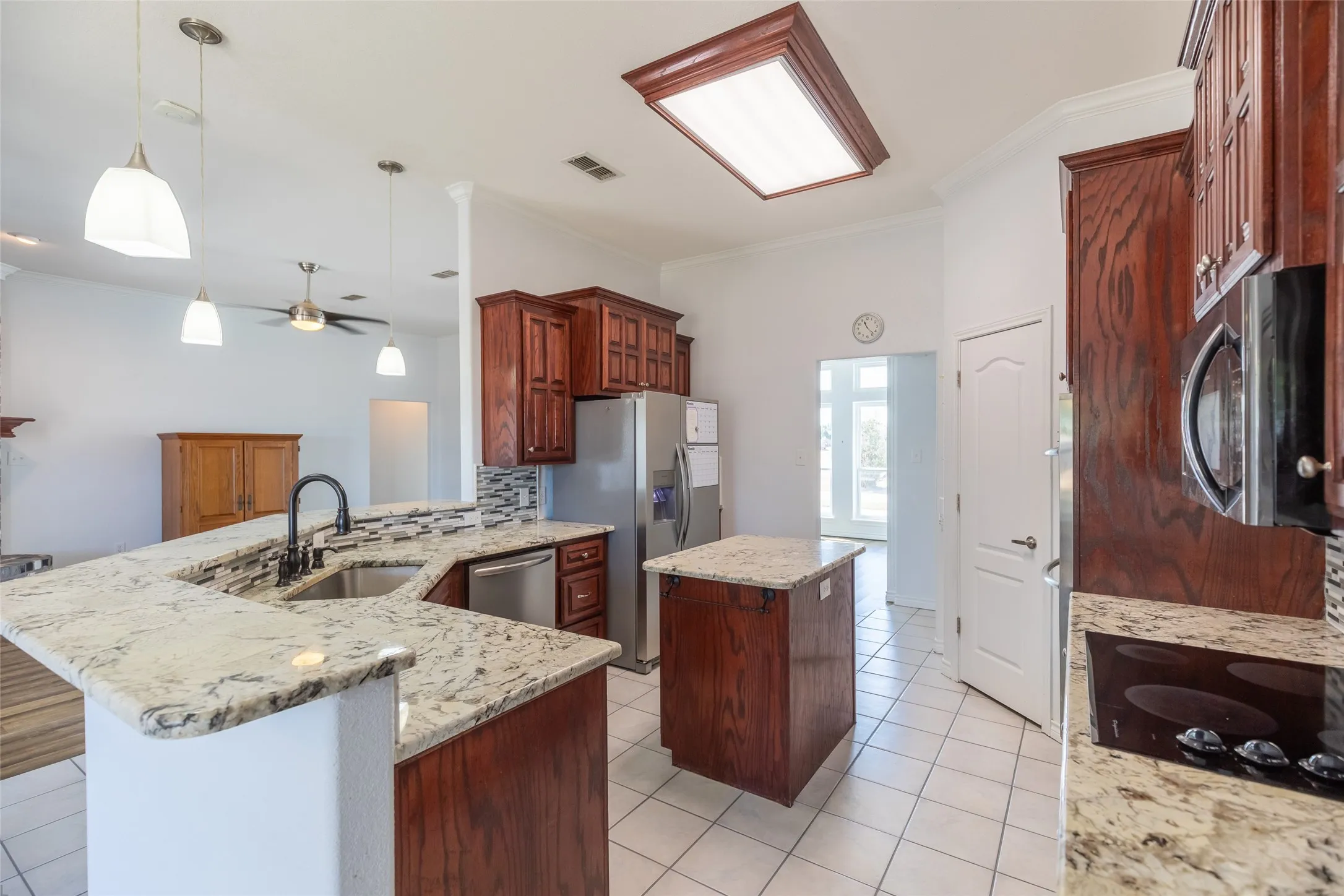Kitchen featuring a large central island, a peninsula with an undermount sink, granite countertops, and wood cabinetry