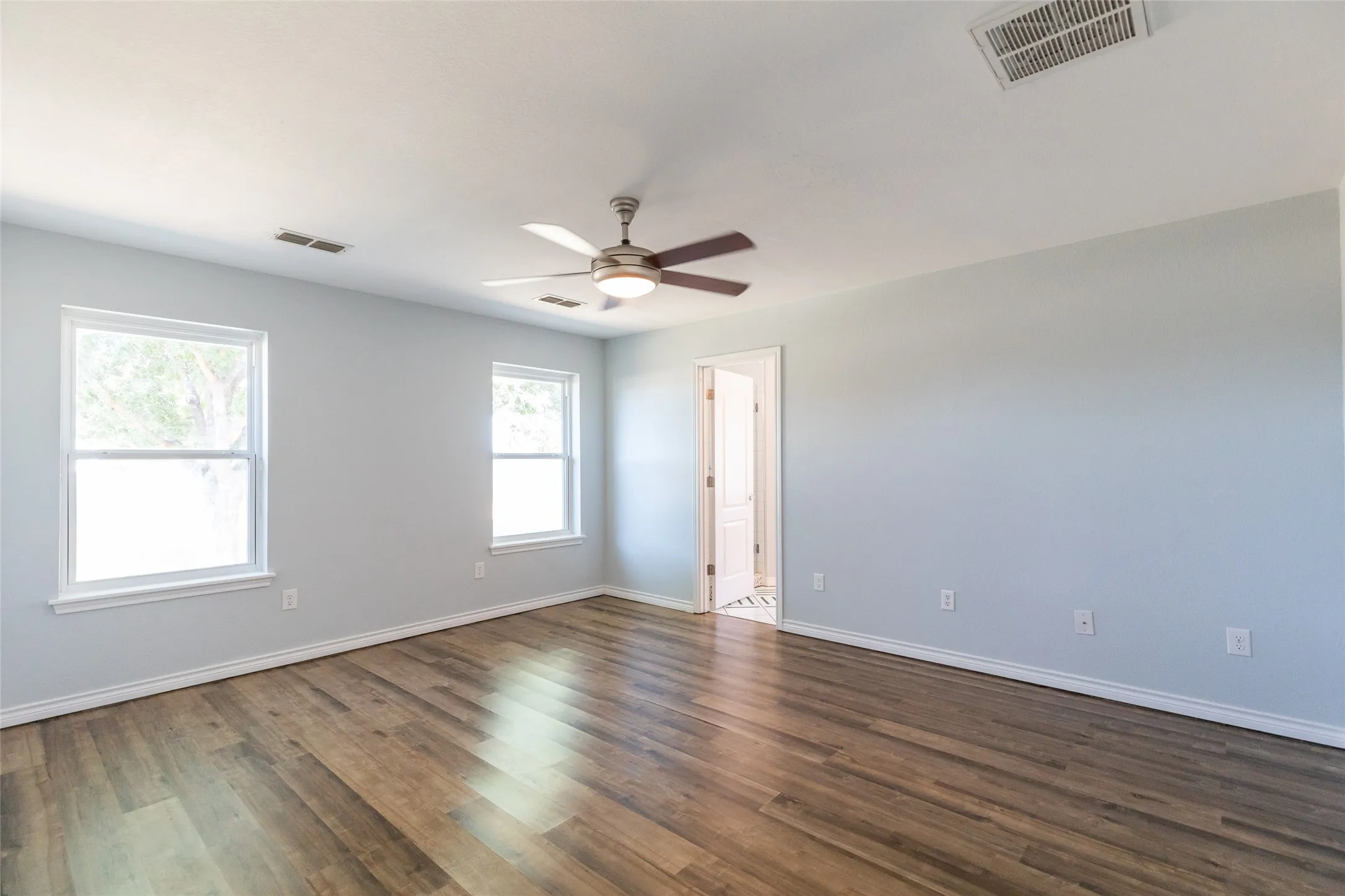 Wood-finish flooring, two large windows with white trim, and a ceiling fan with integrated lighting