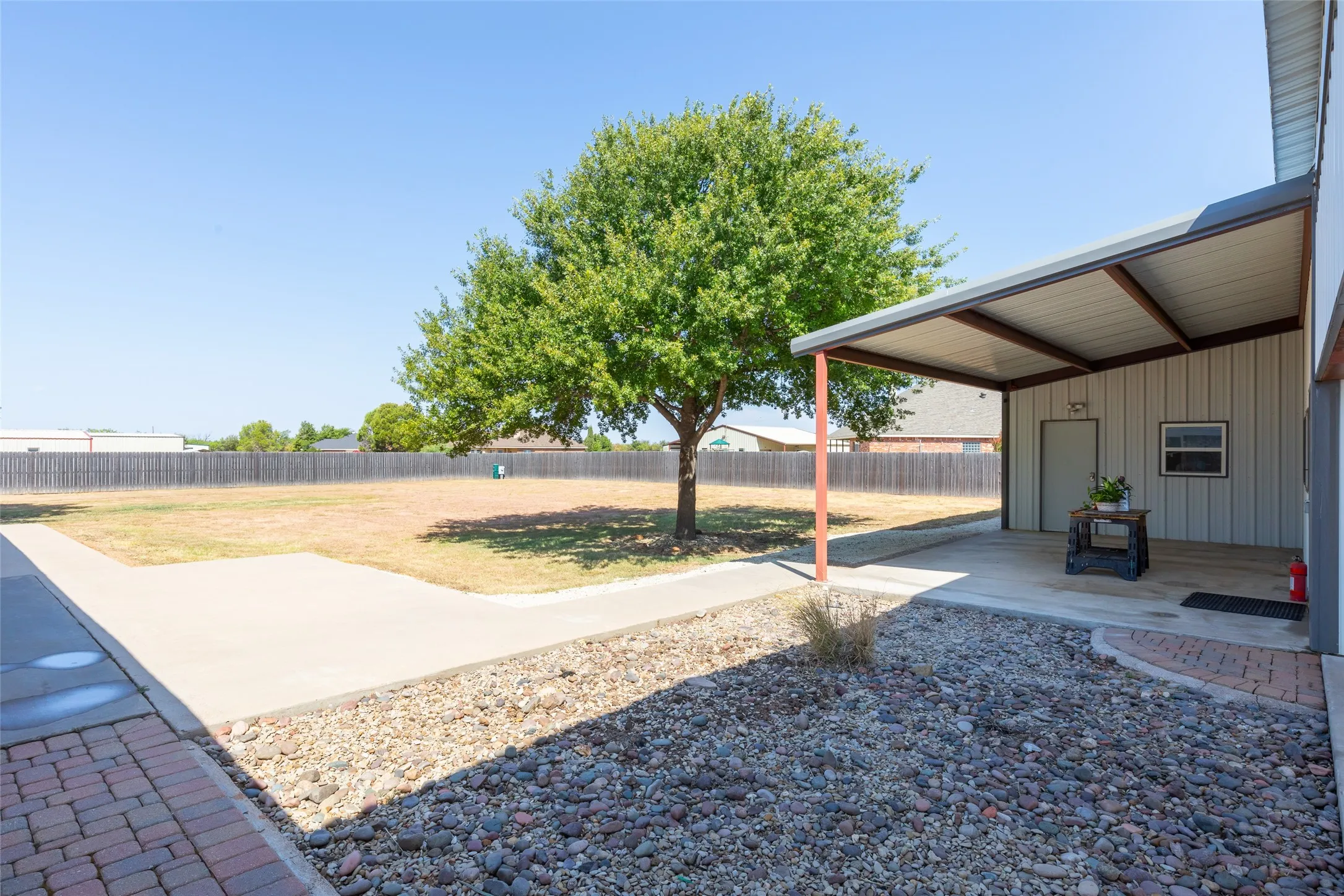 Spacious yard with a mature tree, concrete patio, covered outdoor area, and a privacy fence