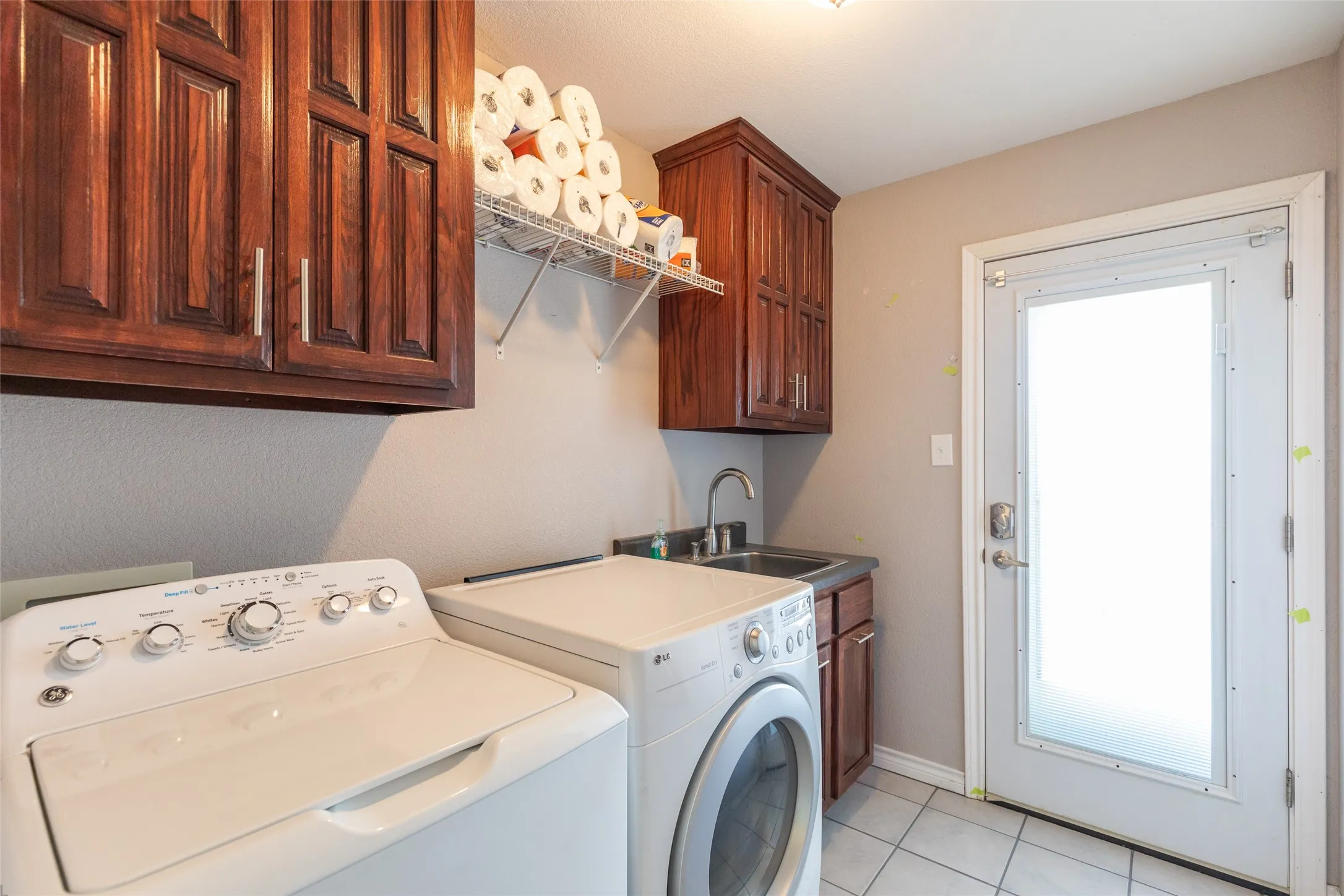 Laundry area featuring rich wood-finish cabinetry, a utility sink with a chrome faucet, and tiled flooring