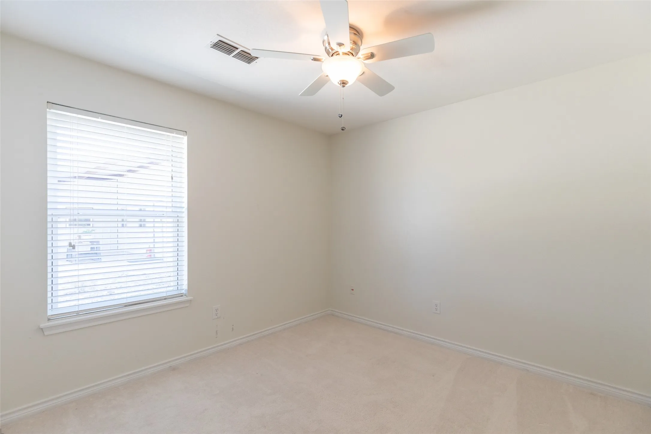 Neutral-toned carpet flooring, light-colored walls, window with blinds, and a ceiling fan with integrated lighting