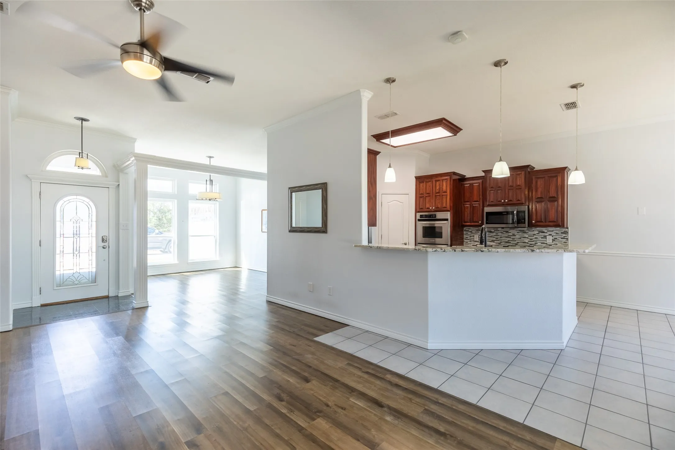 Wood-finish flooring, white tile flooring, recessed lighting, ceiling fan, and a kitchen featuring wood cabinetry with stainless steel appliances