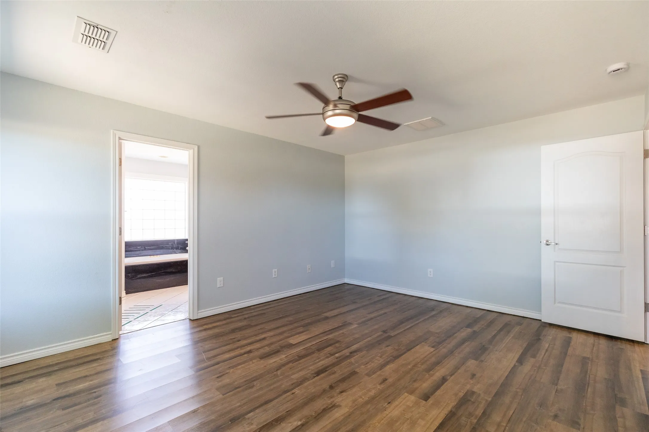 Wood-finish flooring, light-toned walls, and a ceiling fan with integrated lighting