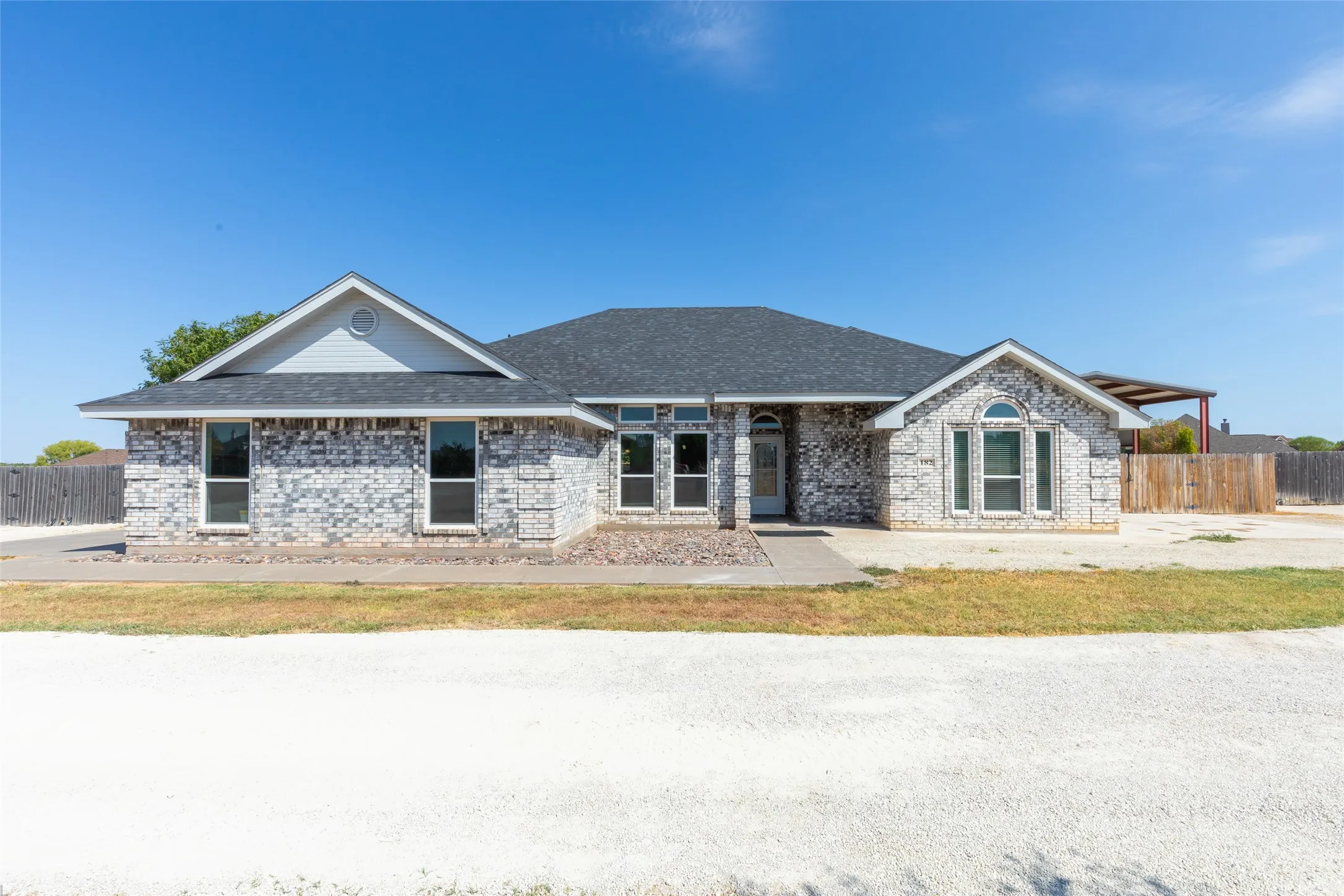 Light-colored brick exterior with decorative stone accents, dark shingle roof, arched and rectangular windows, and a covered entry