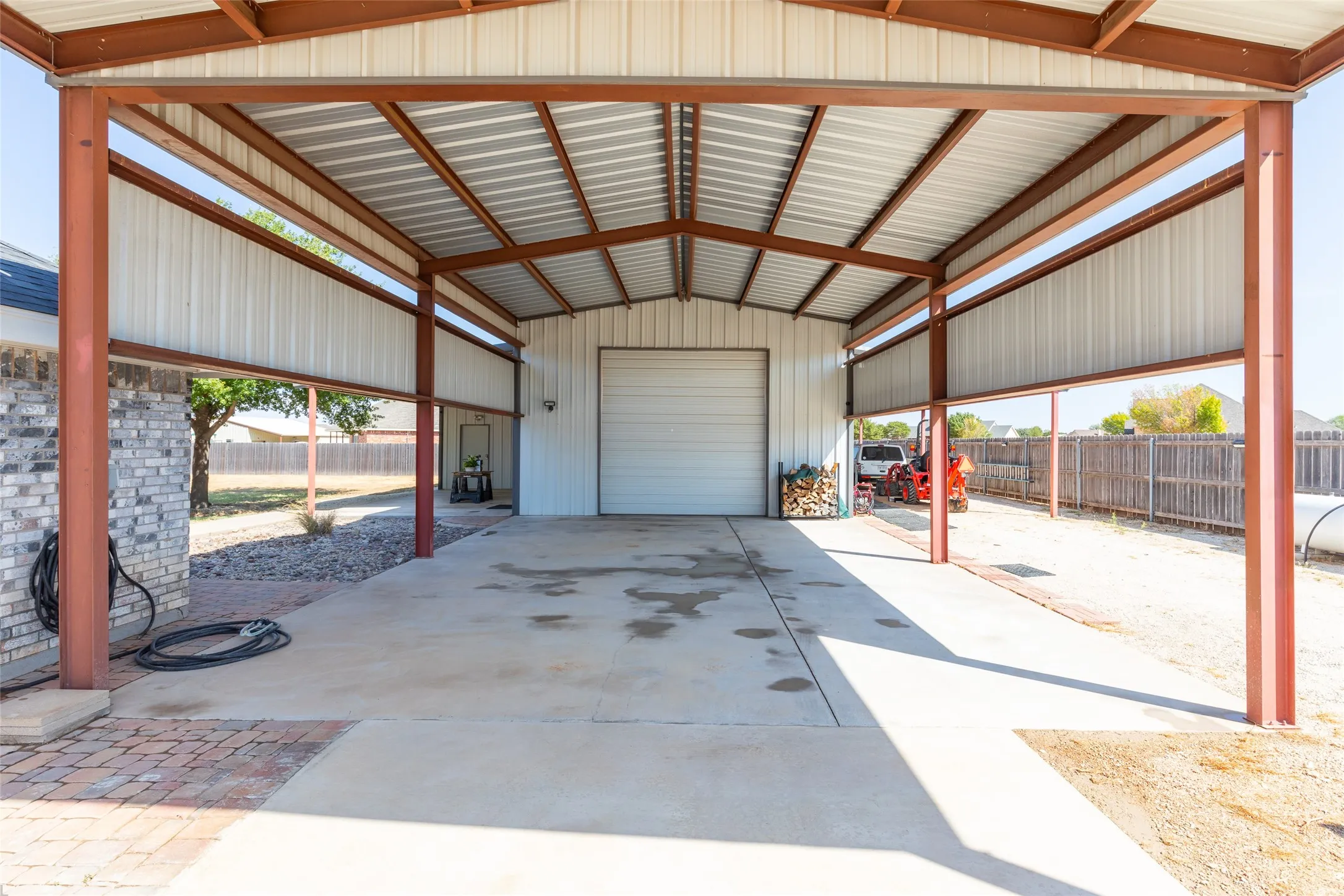 Attached metal carport featuring a concrete pad and a roll-up garage door on the adjacent structure