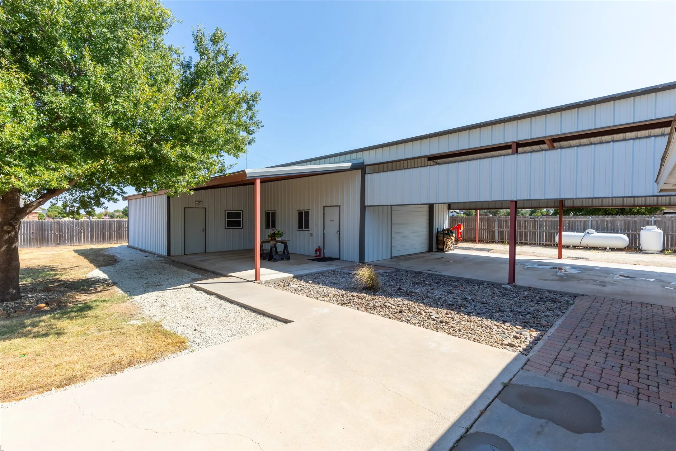 Metal-sided structure featuring multiple entry points, a covered concrete patio, and an integrated carport area with a roll-up door