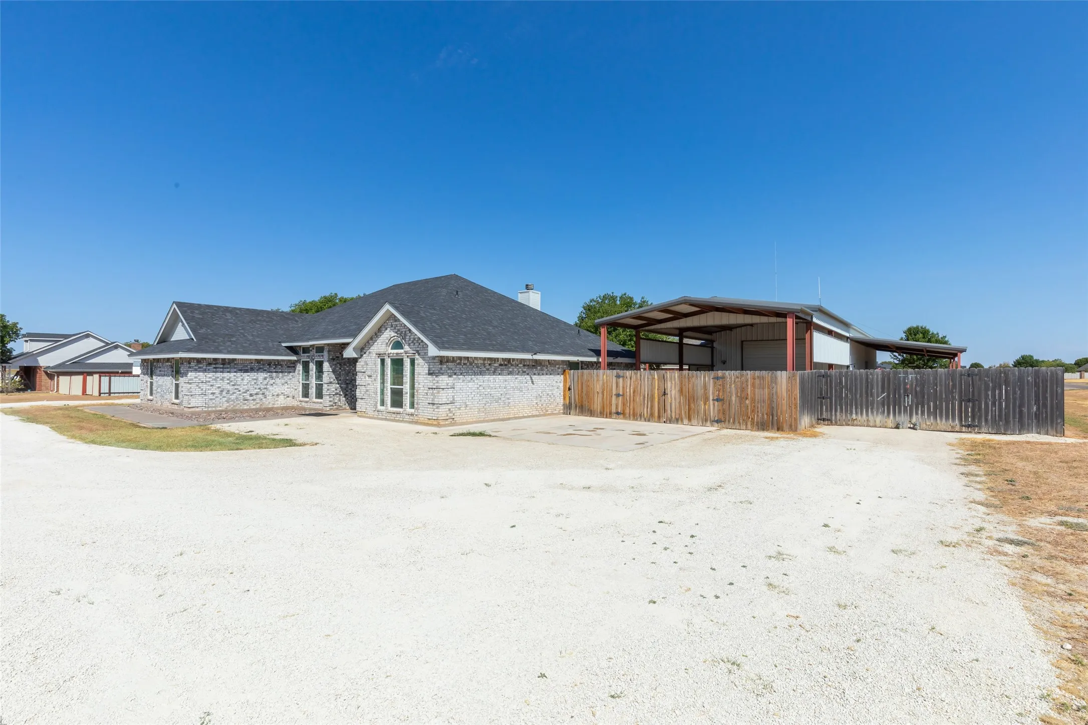 Brick exterior residence with a dark shingle roof, arched transom windows, and an expansive gravel driveway