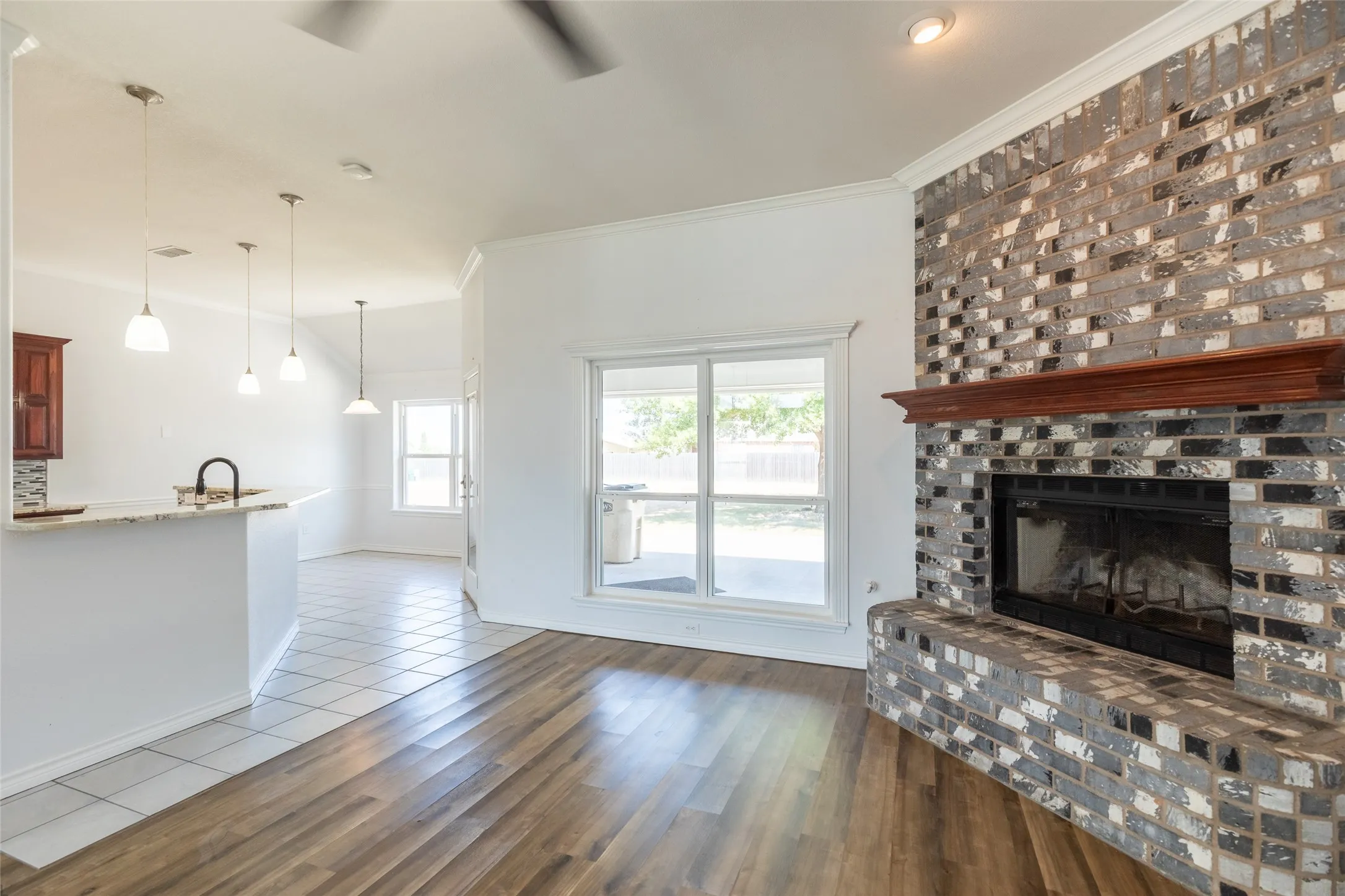 Wood-finish flooring, brick fireplace with wood mantel, large windows, and pendant lighting