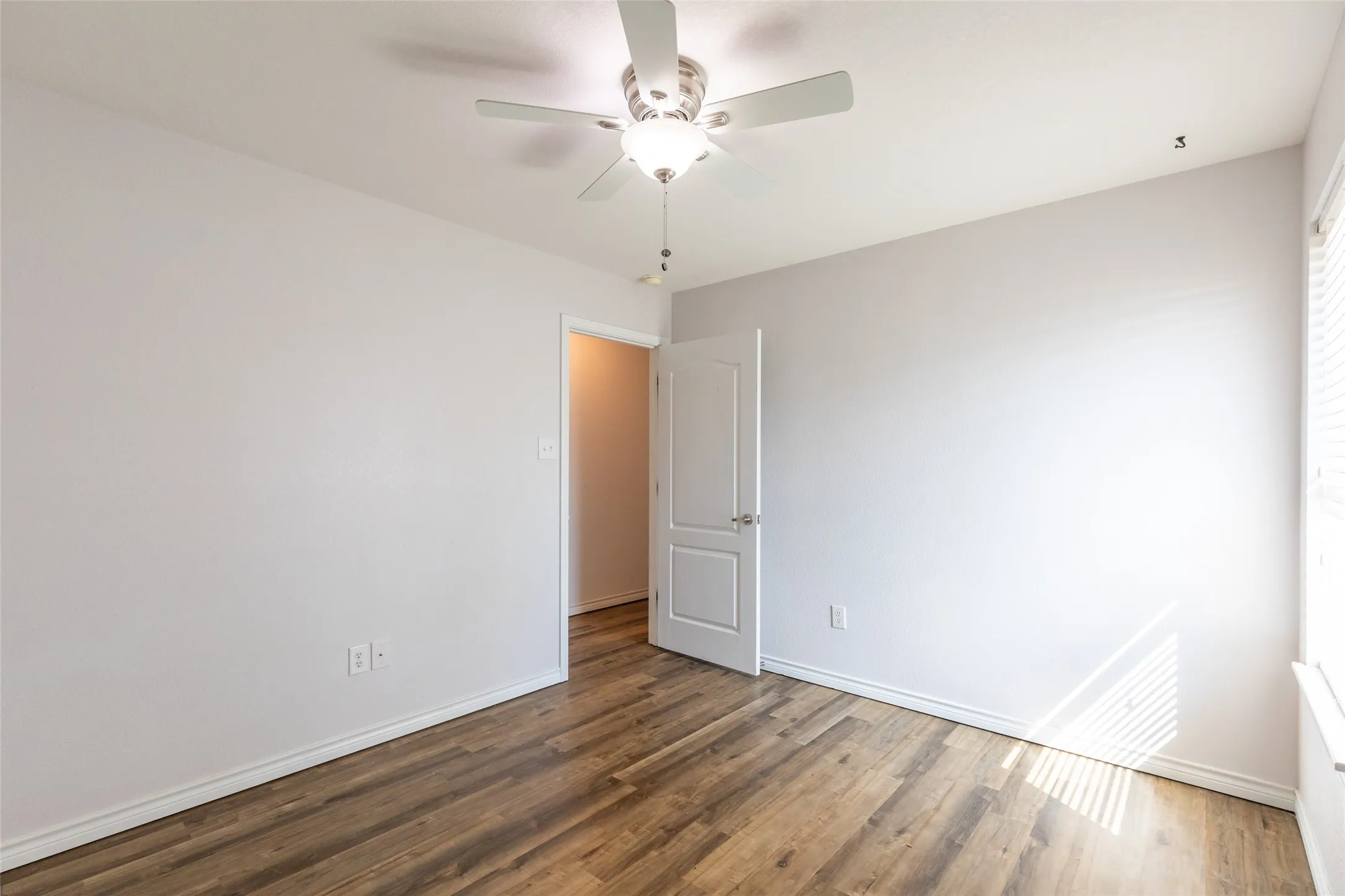 Wood-finish flooring, ceiling fan with integrated lighting, white interior door, and window with blinds