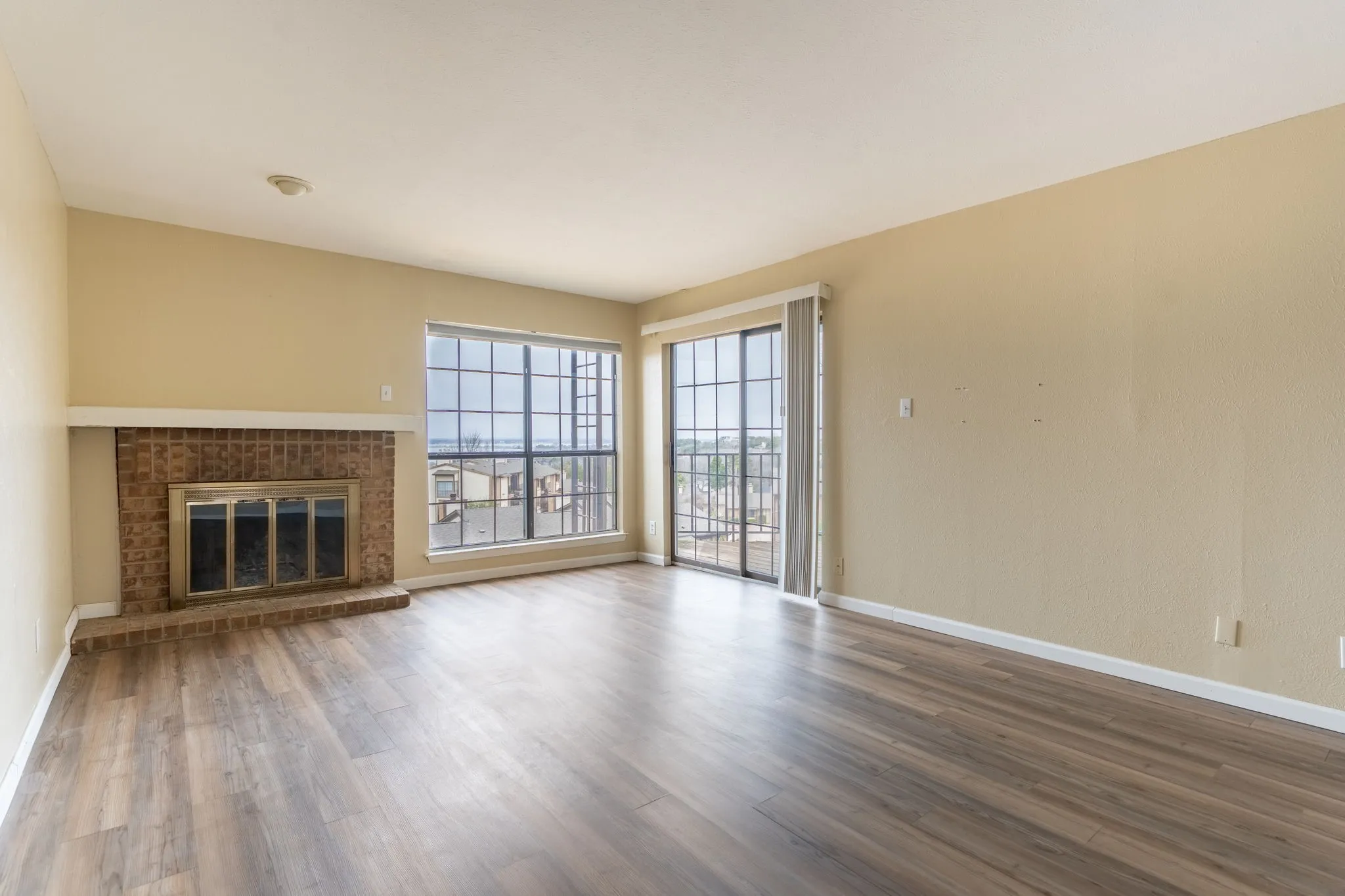 Living area featuring wood-finish flooring, a brick fireplace with a mantle, large grid windows, and a sliding glass door