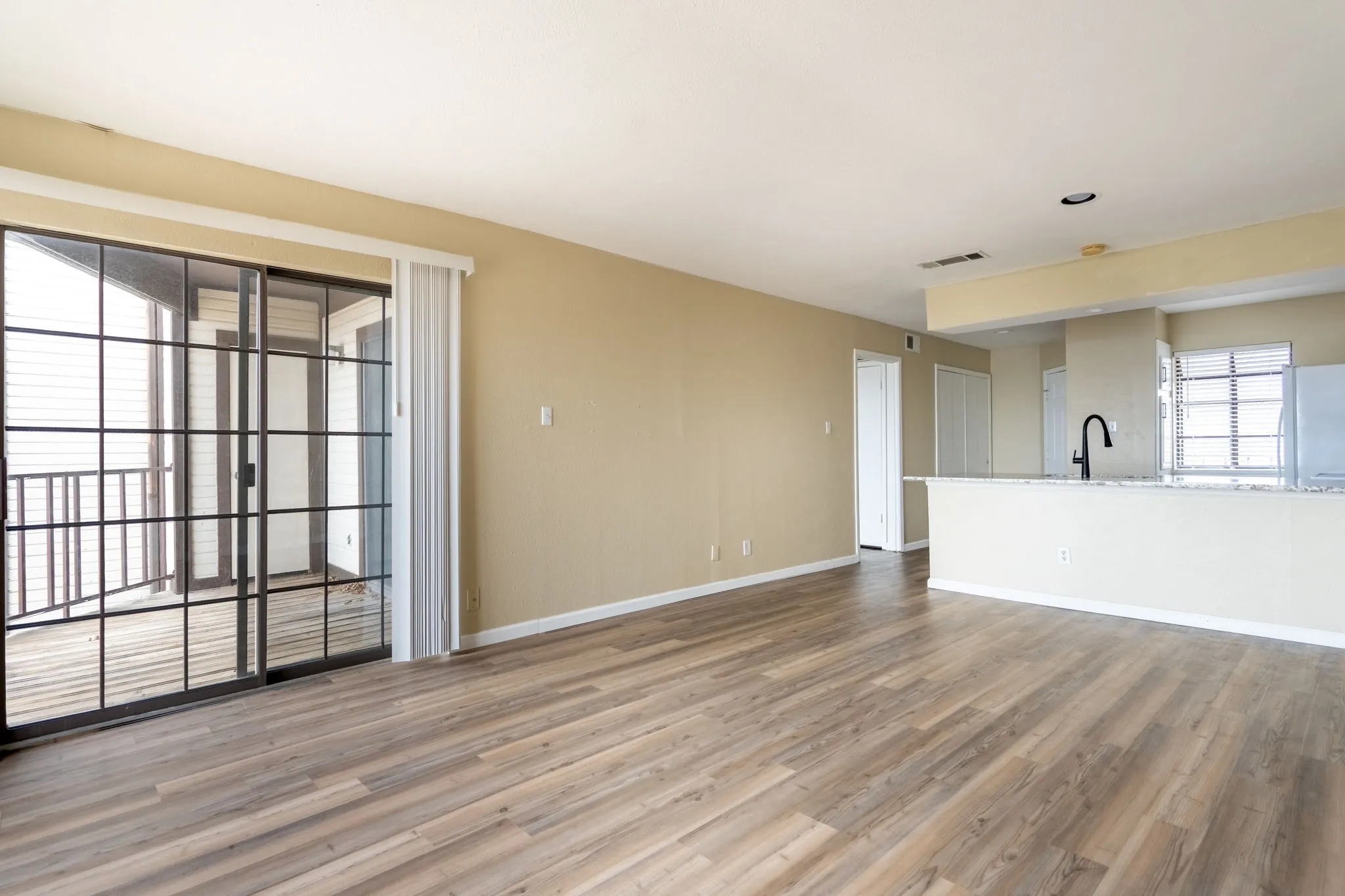 Wood-finish flooring throughout, sliding glass door with balcony access, kitchen with a breakfast bar, recessed lighting, and a modern black gooseneck faucet