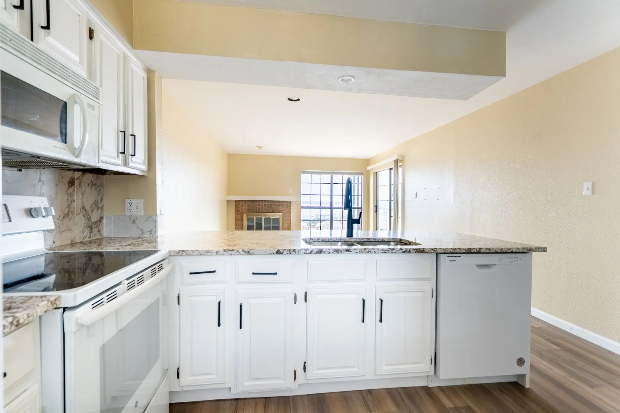 Modern kitchen featuring white cabinetry with brushed nickel hardware, granite countertops, stainless steel appliances including a gas cooktop and built-in microwave, and wood-finish flooring throughout