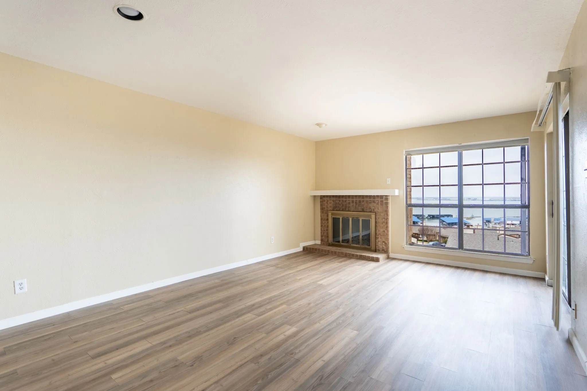 Wood-finish flooring, recessed lighting, brick fireplace with mantel, large picture window with water scenery, and a split air conditioning unit