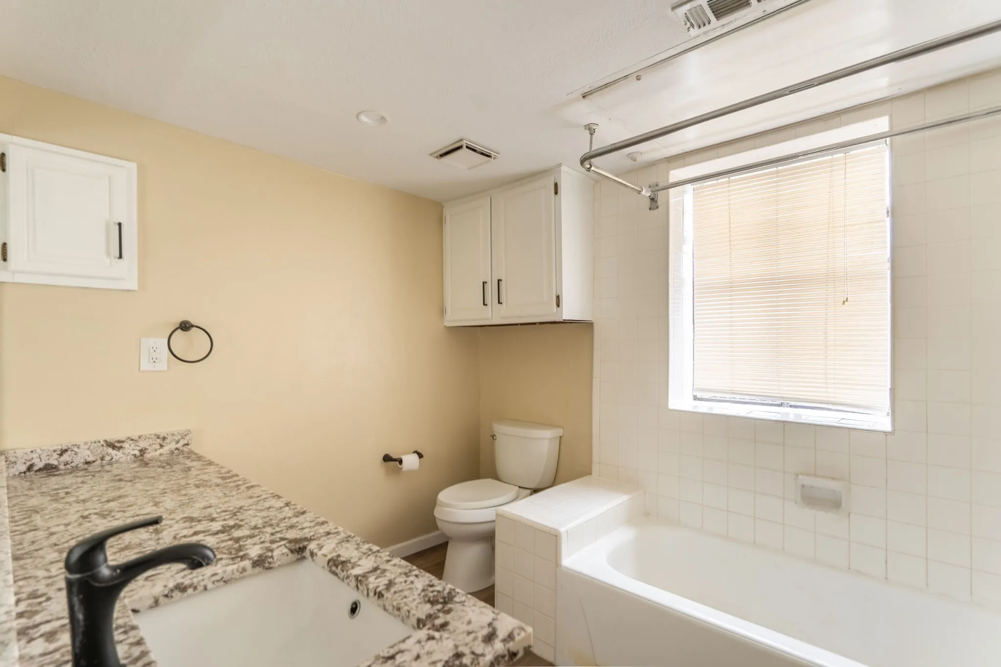 Granite-style countertop, integrated sink, matte black faucet, and white tiled bath surround