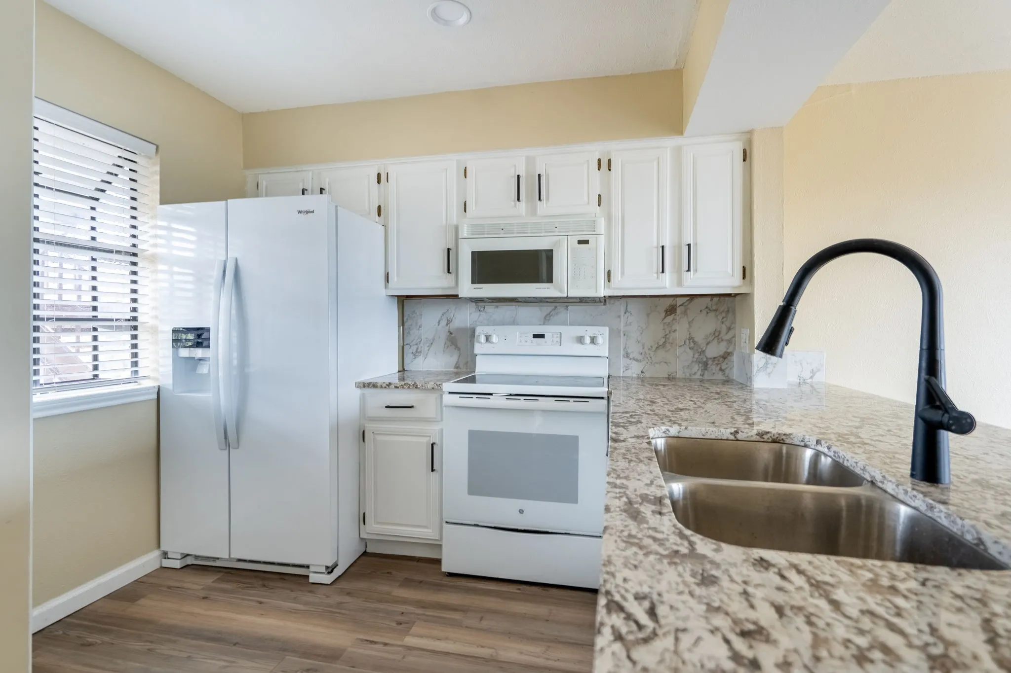 Kitchen featuring white cabinetry, wood-finish flooring, stone-look countertops, a double basin sink with a matte black faucet, and white appliances