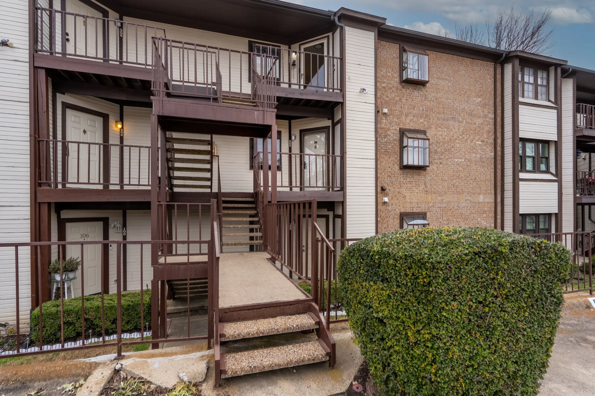 Multi-level building with brick and siding exterior, featuring dark brown railings and stairs